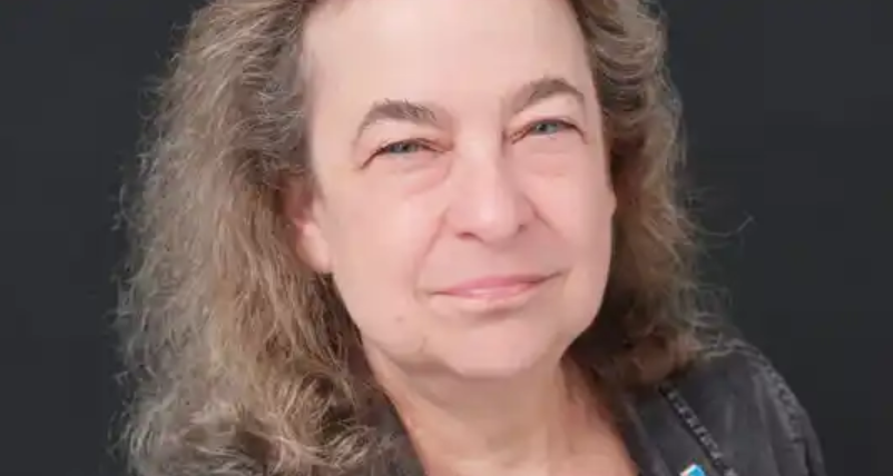 Portrait of a middle-aged woman with curly blonde hair, smiling slightly, against a dark background.