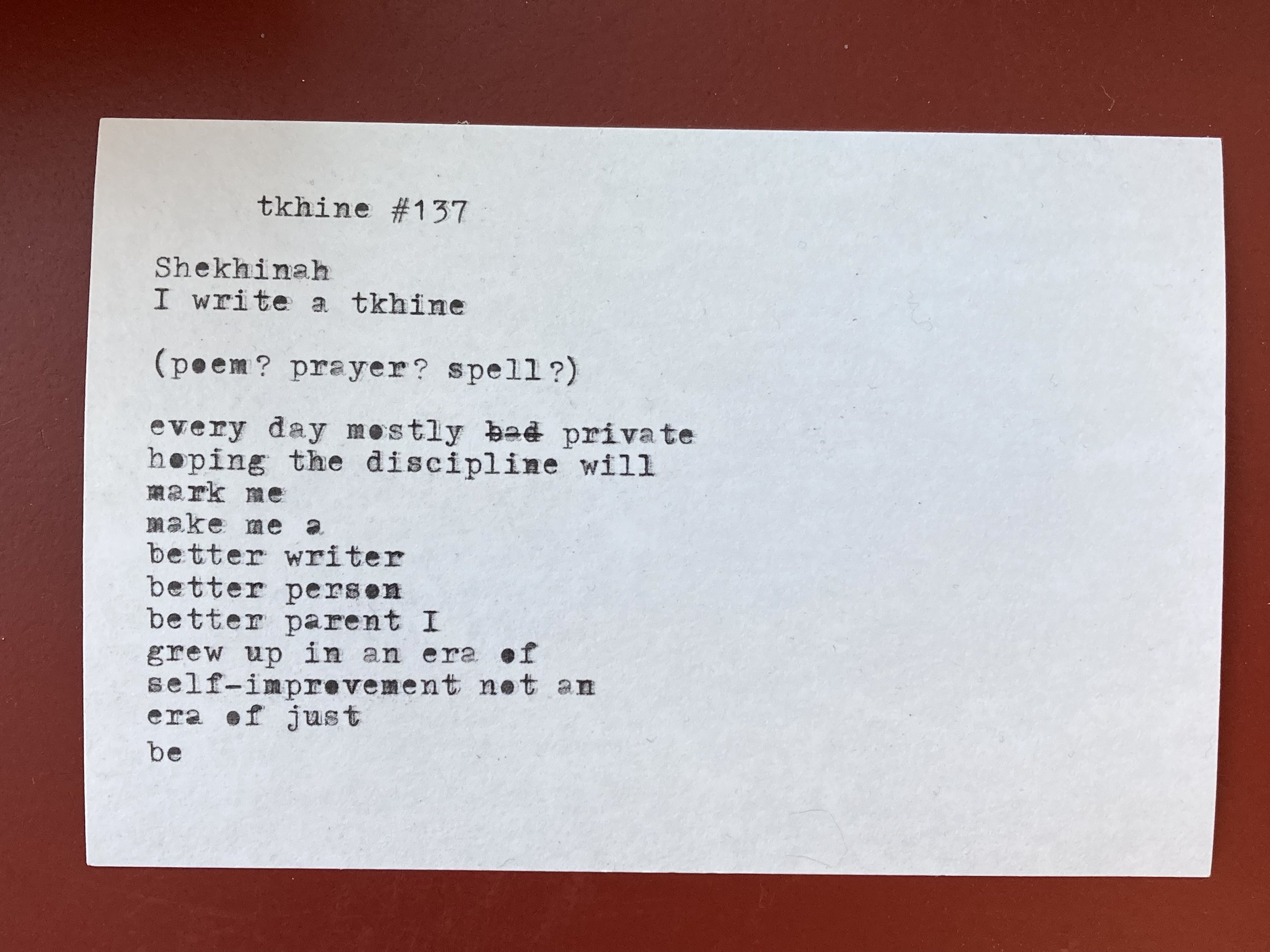 A typed poem titled 'tkhine #137' on a white sheet of paper, placed on a red surface. The poem references Shekhinah and expresses a personal desire for self-improvement.
