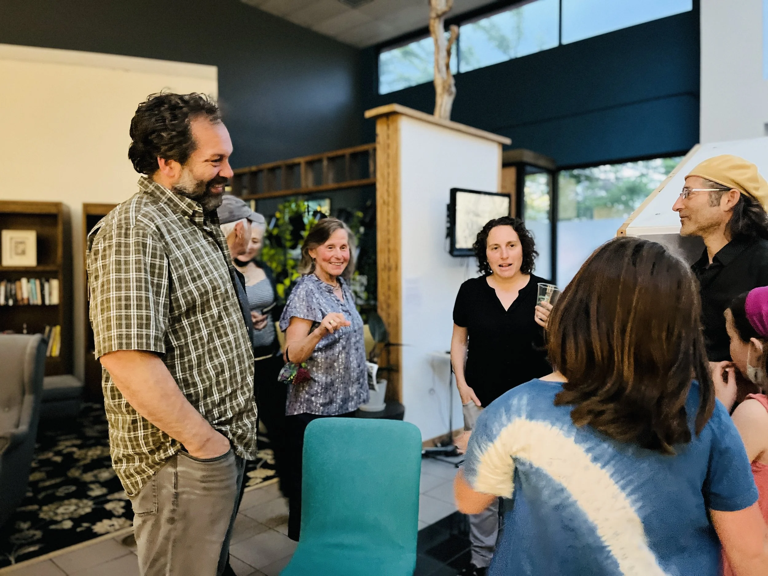 Group of people talking and laughing in an indoor setting, with some holding drinks, during a social gathering or celebration.