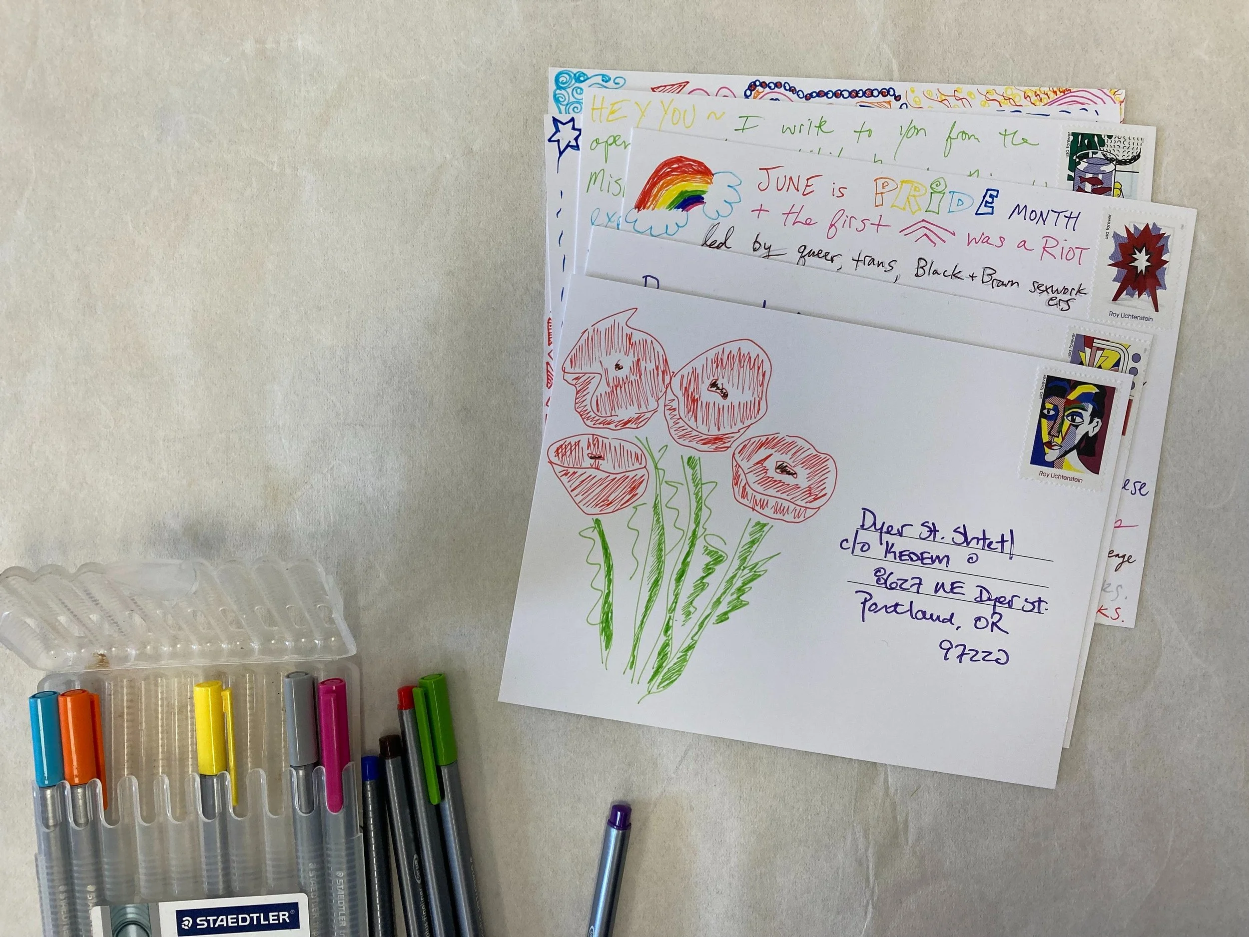 Colorful handwritten postcards and a floral drawing with markers on a light surface.
