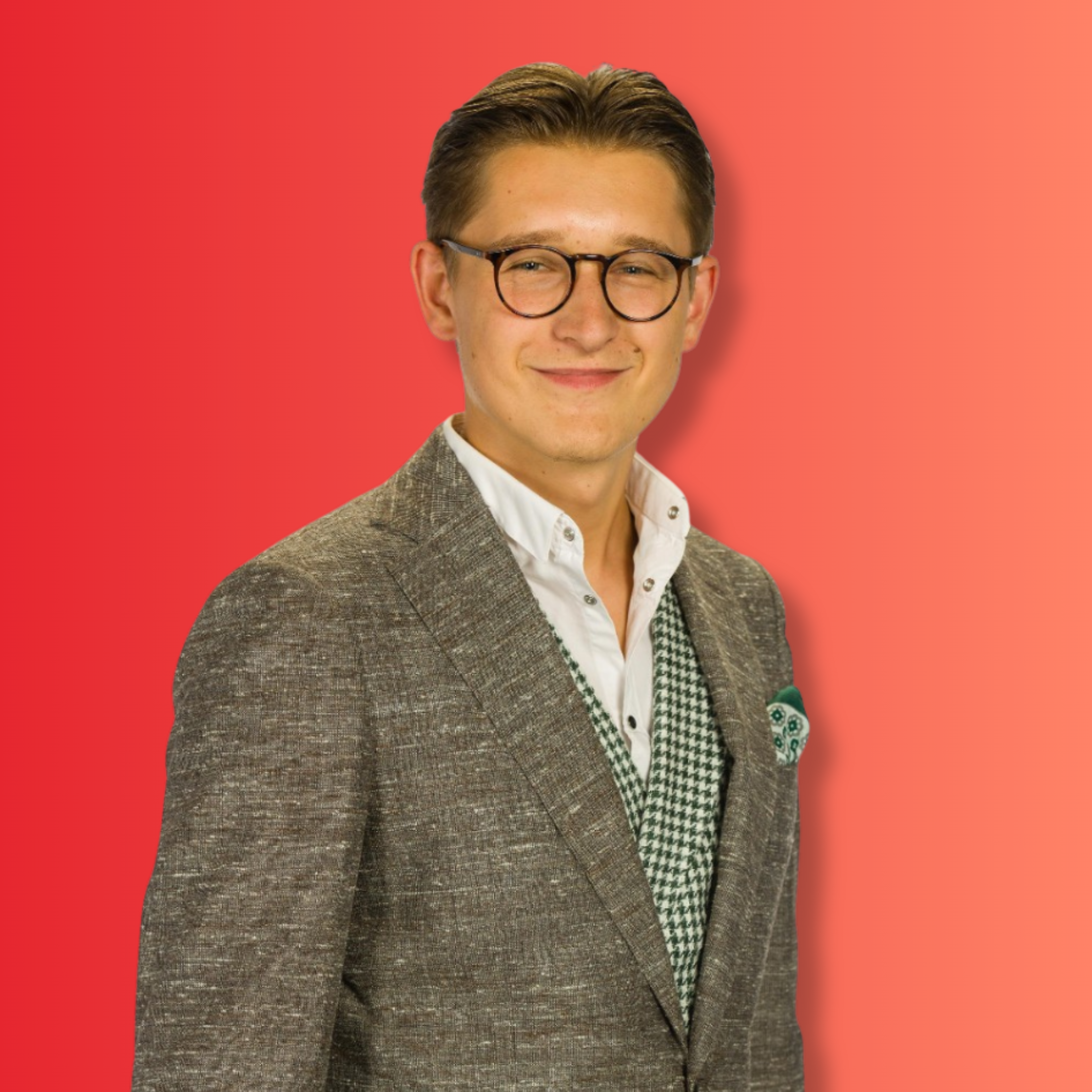 Ein junger Mann mit Brille, Hemd, Pullover und Jacke vor einem roten Hintergrund.