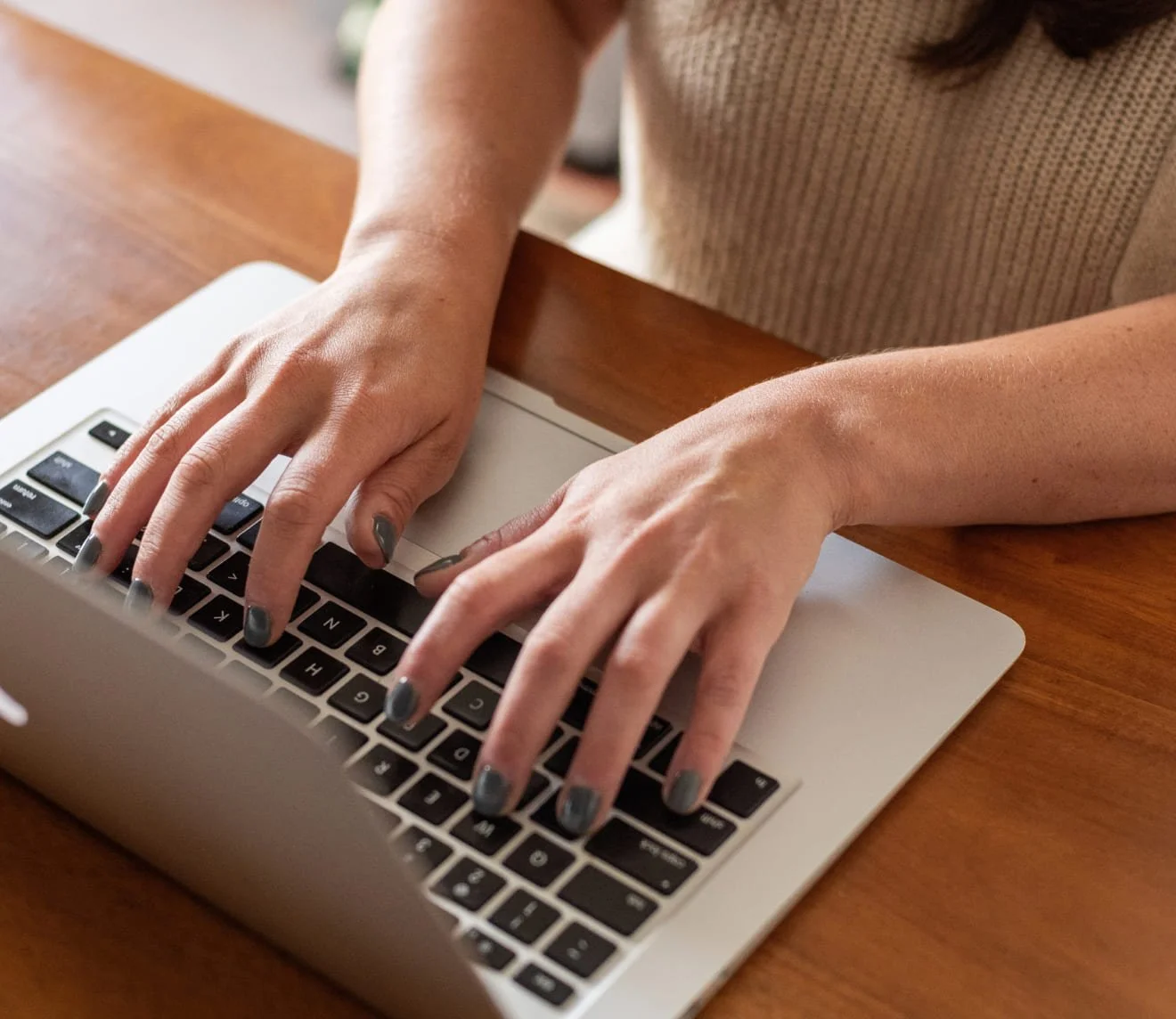 Person typing on a silver laptop with black keys, sitting at a wooden table.