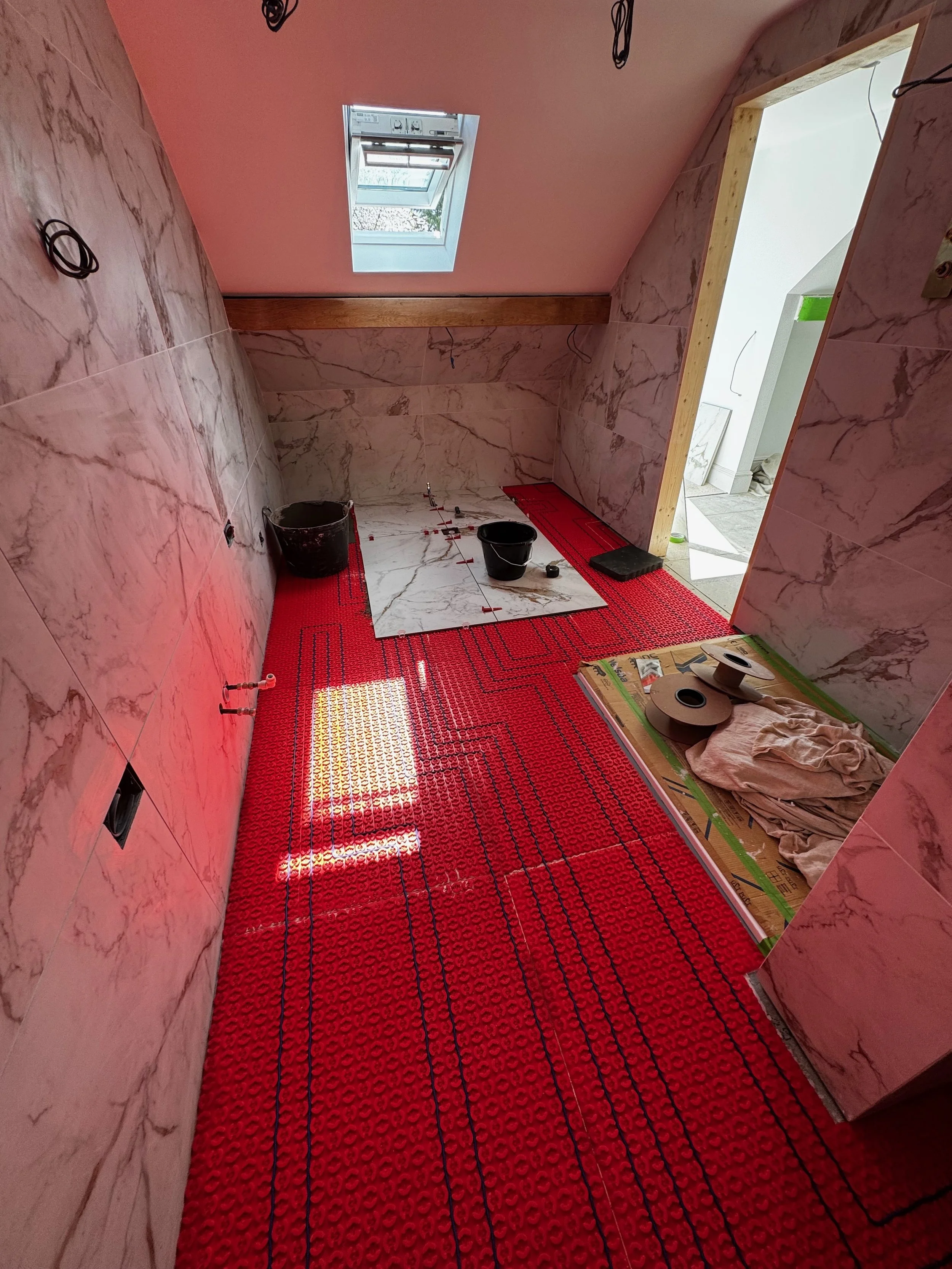 Bathroom under renovation with red underlayment, marble wall tiles, a skylight window, and construction tools and materials on the floor.
