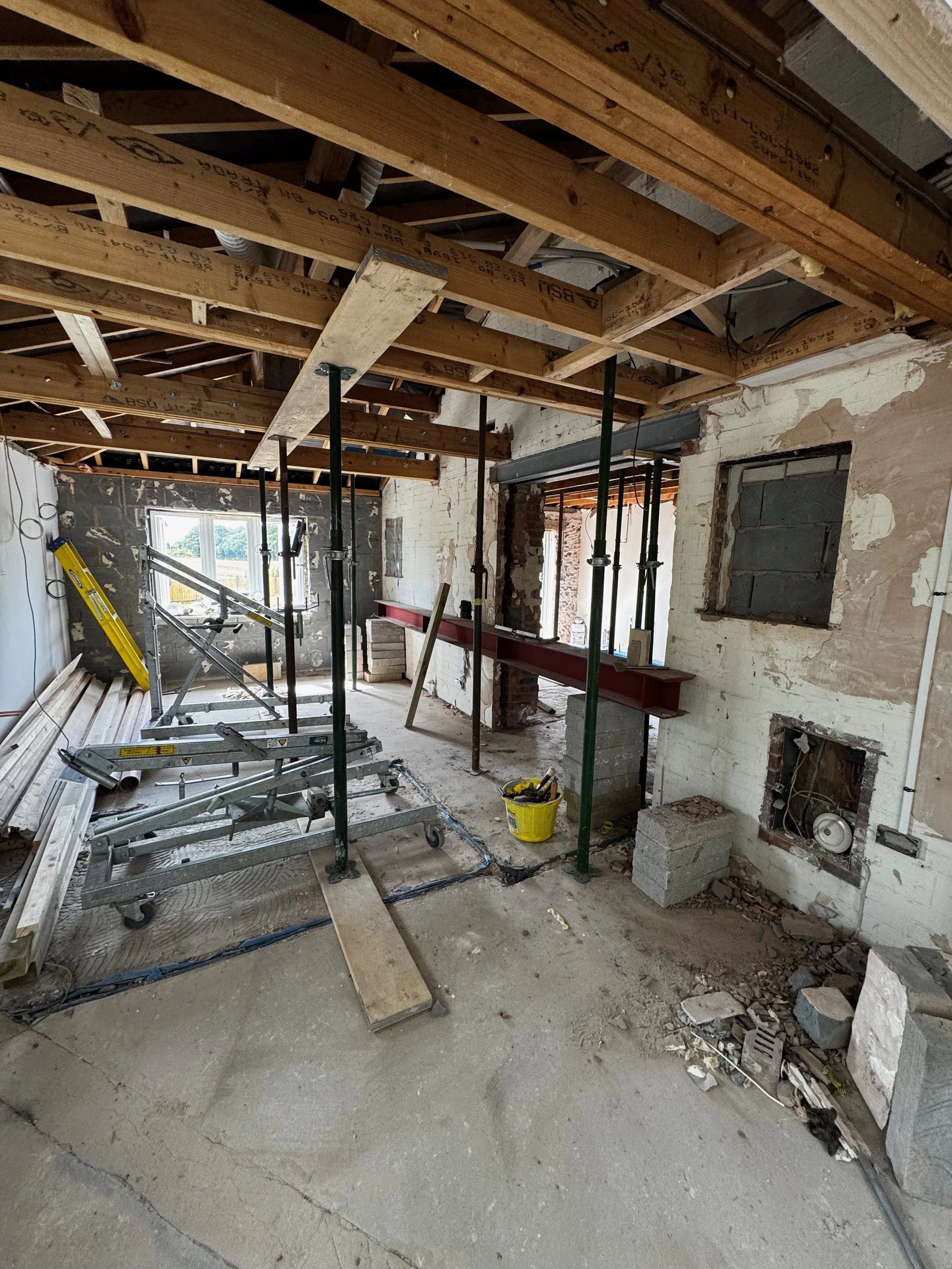 Interior of a house under renovation with exposed ceiling beams, construction scaffolding, and unfinished walls.