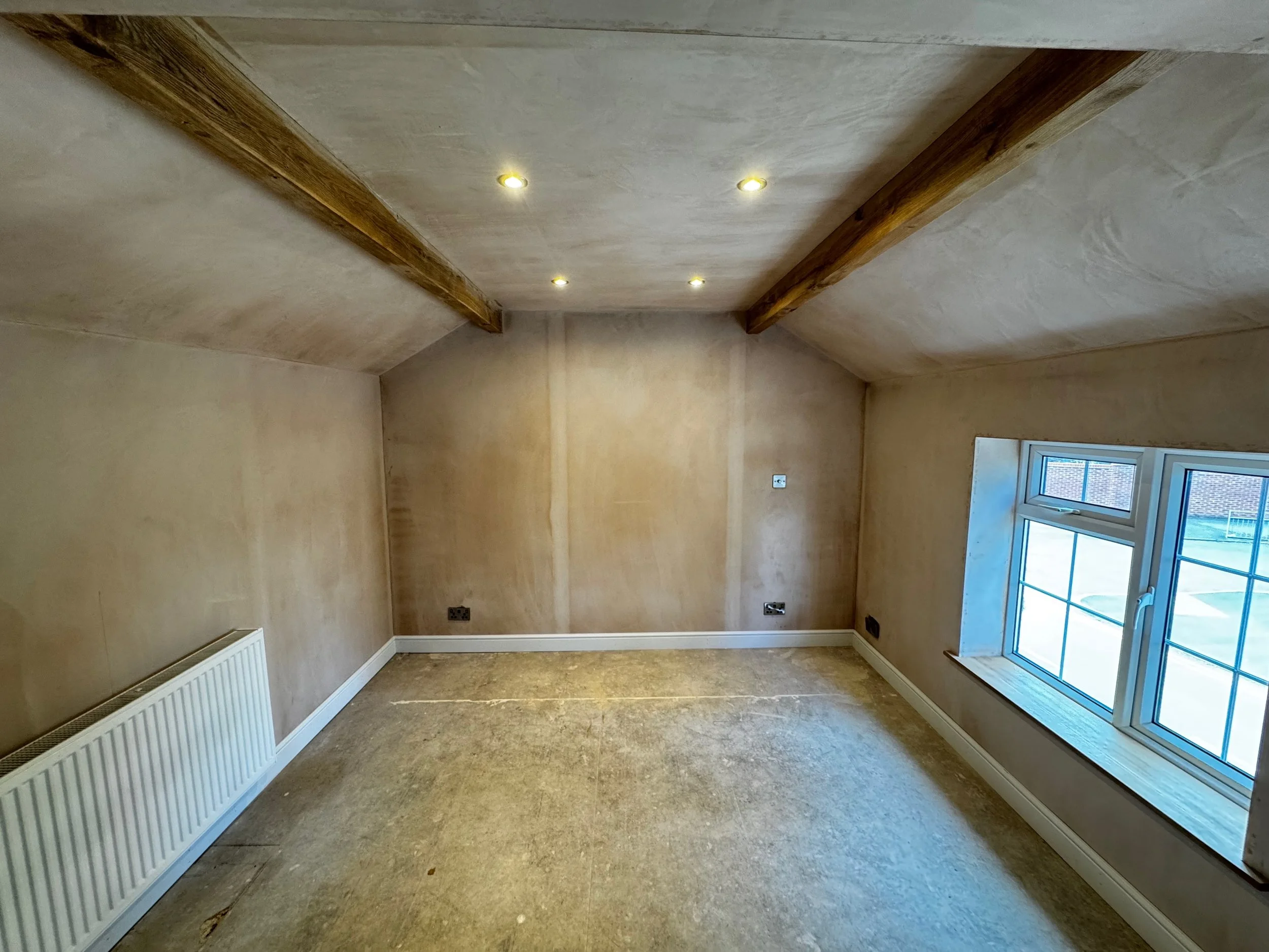 Remodelled and plastered bedroom,  wooden beams on the ceiling, a window on the right wall, and recessed ceiling lights.