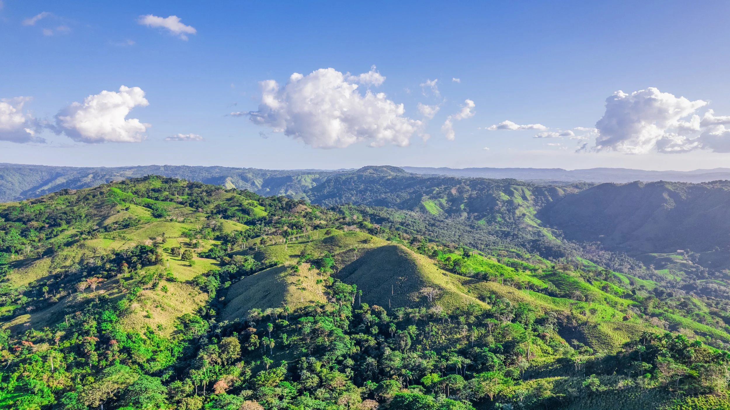 Scenic view of lush green hills and valleys under a partly cloudy sky.