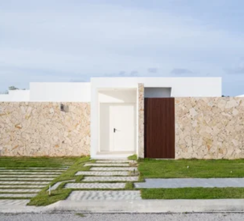 Modern house exterior with a stone wall, white door, and a wooden gate, with a pathway and green lawn in front.