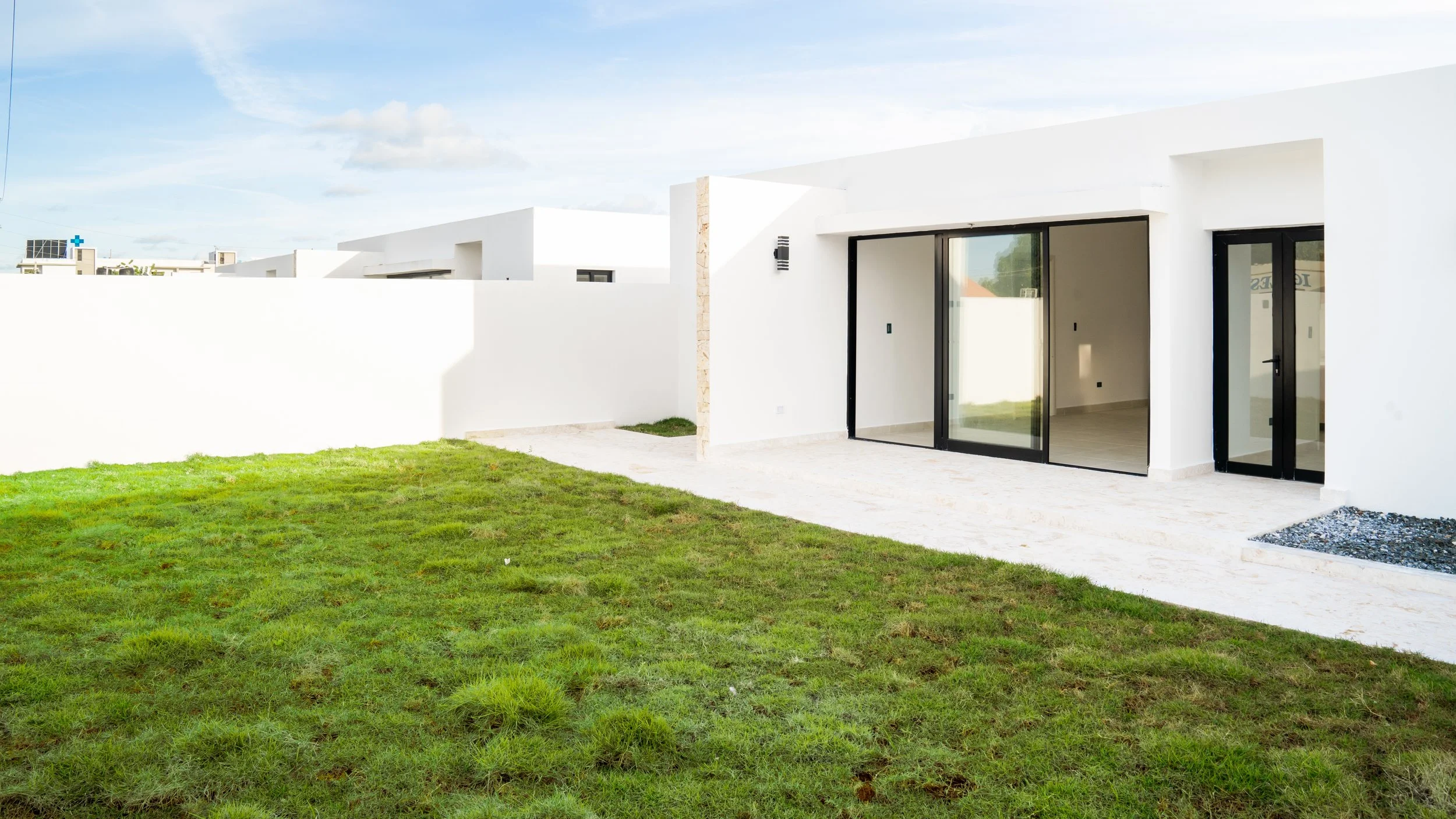 Modern white house with large glass sliding doors and a grassy backyard.