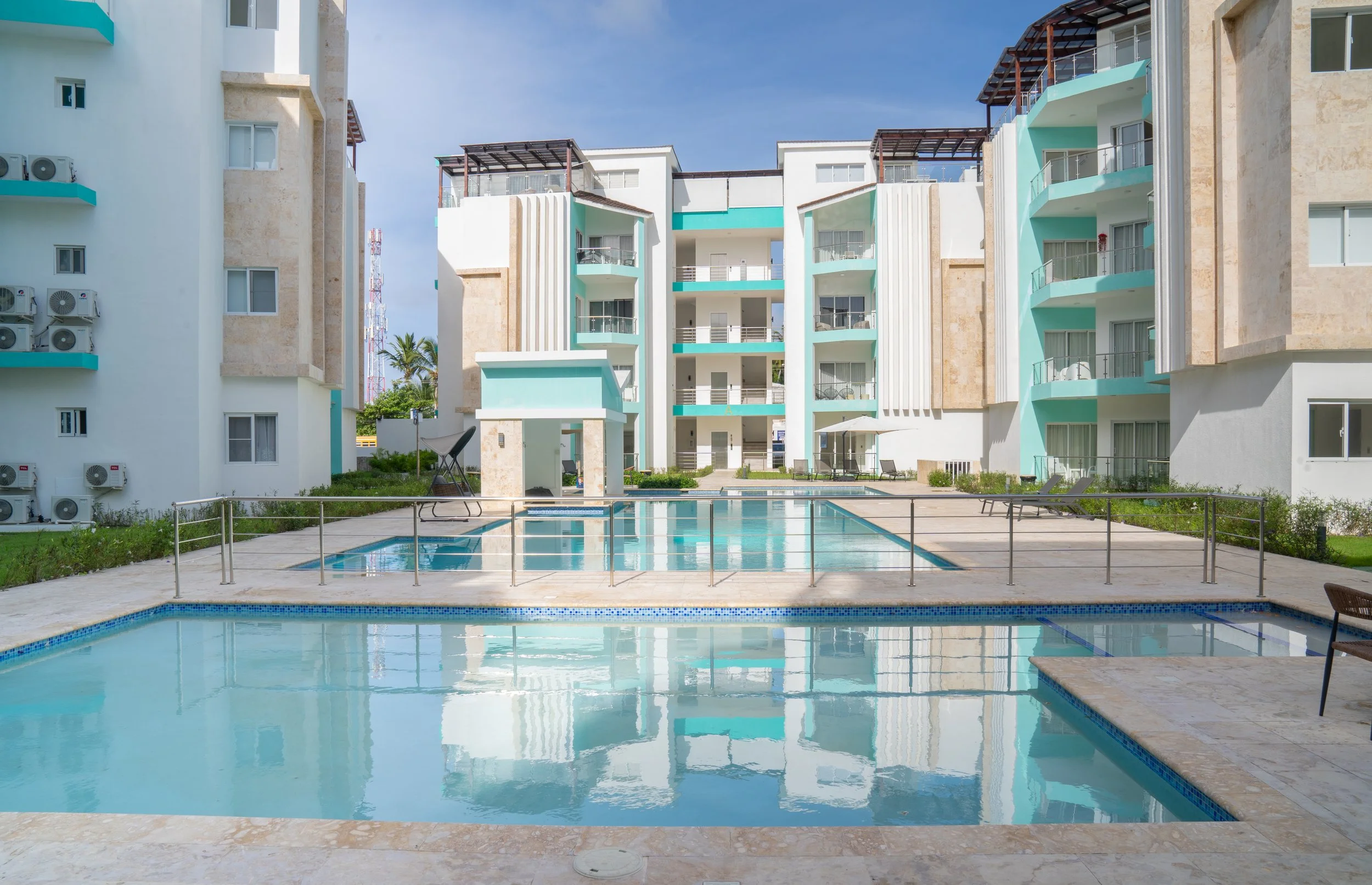 View of a modern apartment complex with outdoor swimming pools and balcony units under a blue sky.