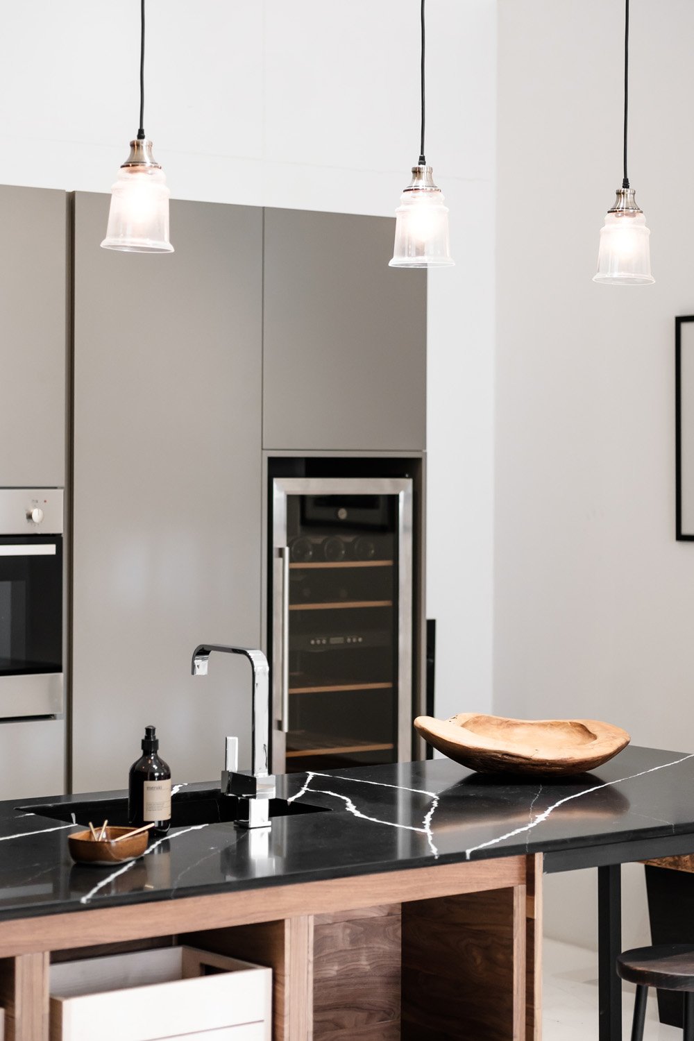 Modern kitchen with gray cabinets, black marble countertop, wooden island, pendant lights, and built-in wine cooler.