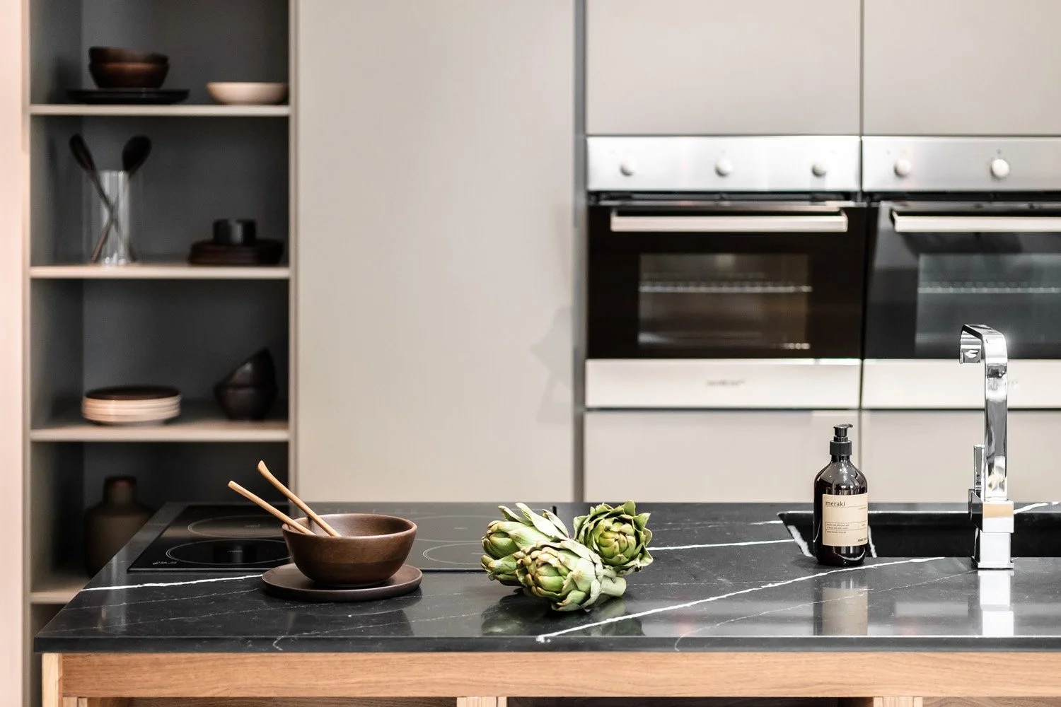 Modern kitchen with black marble countertop, artichokes, brown bowls with chopsticks, a soap dispenser, and built-in ovens.