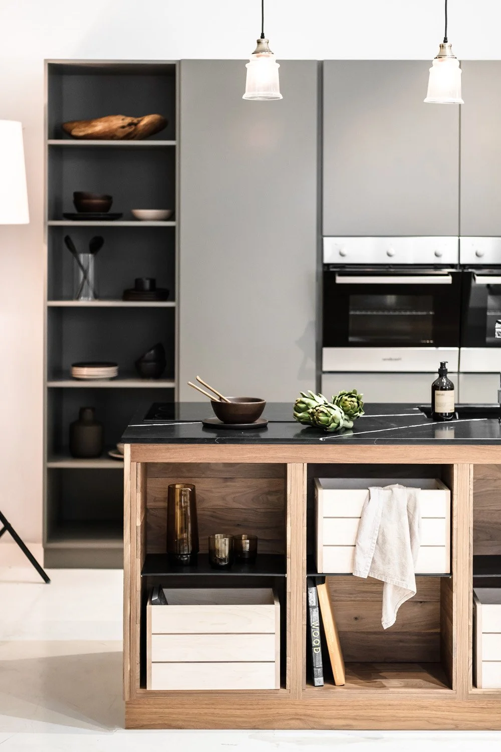 Modern kitchen with gray cabinets, black countertops, open shelving with bowls and decor, and a wooden kitchen island with artichokes, bowls, and a towel.