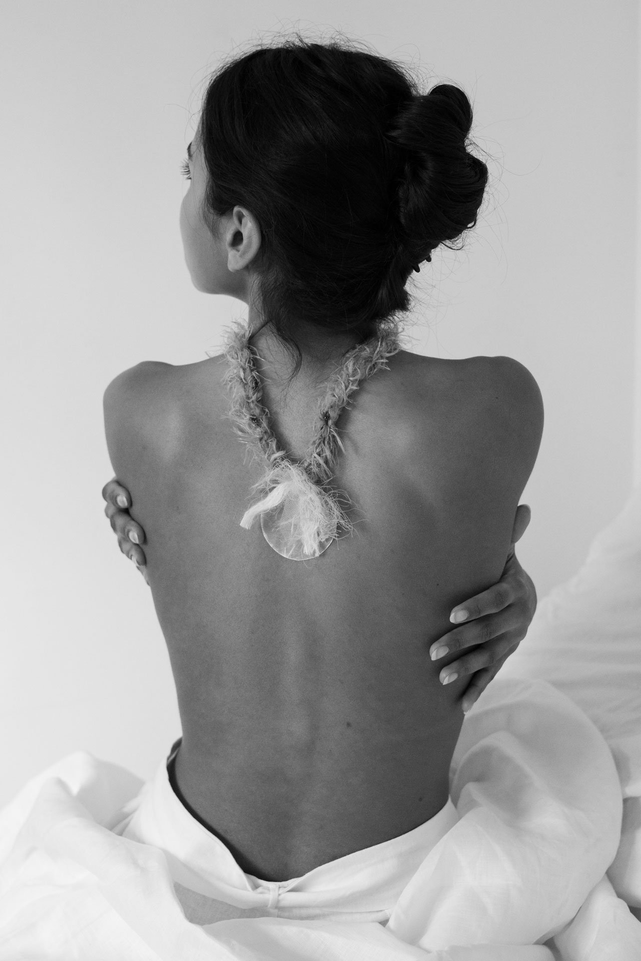A woman with an elegant updo hairstyle, wearing a handmade Arpeggi necklace from the brand Nibi, in a monochrome photograph.