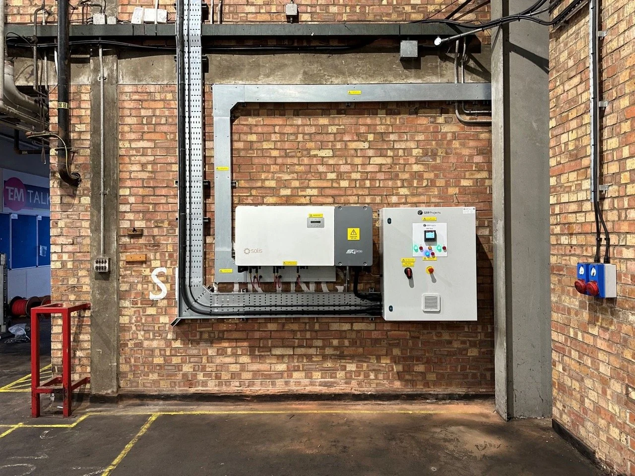 Electrical control panels and conduit wiring mounted on a brick wall in an industrial setting.