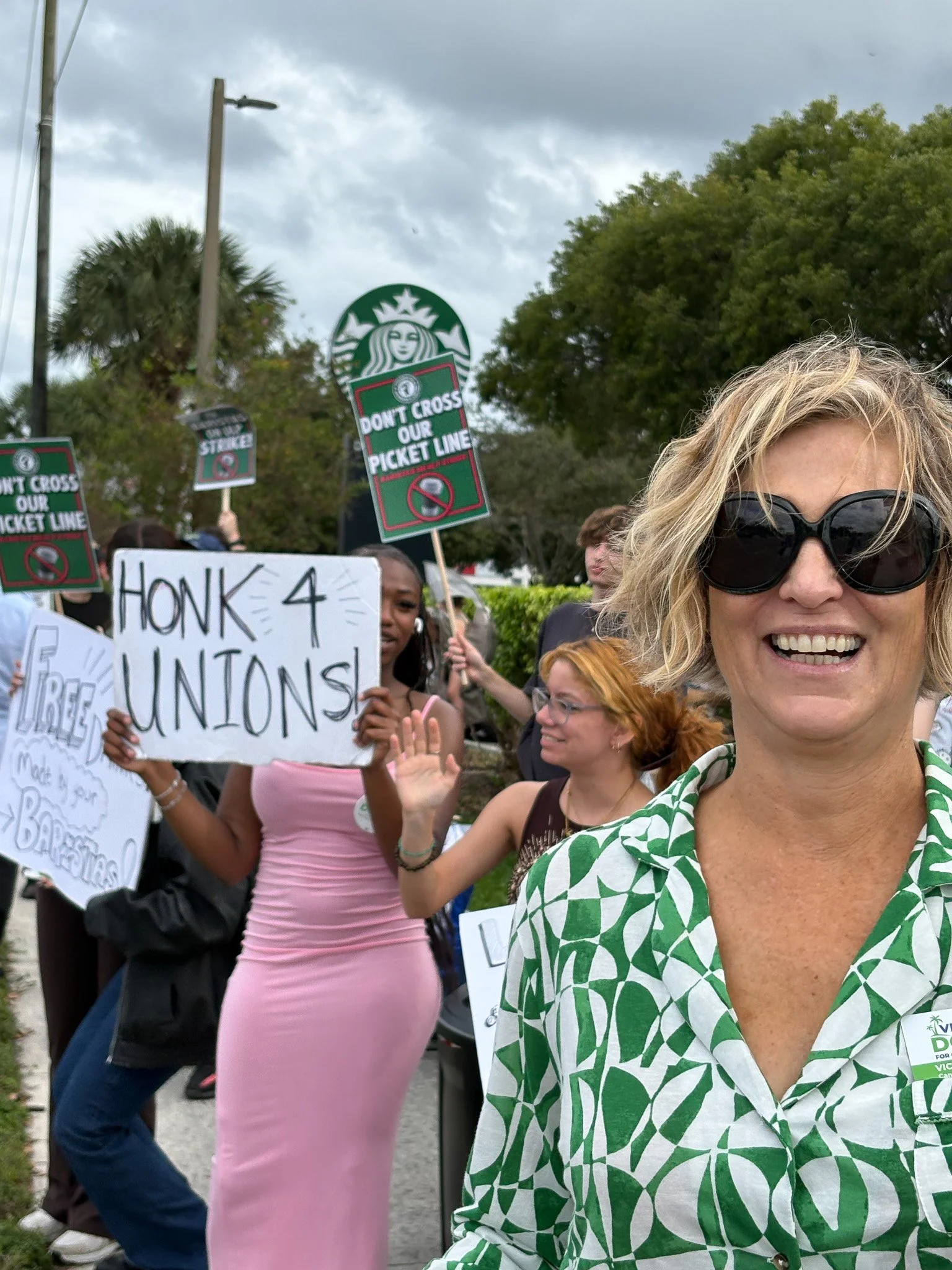 Protesters holding signs that say 'HONK 4 UNIONS' and other signs that say 'DON'T CROSS OUR PICKET LINE' during a demonstration.