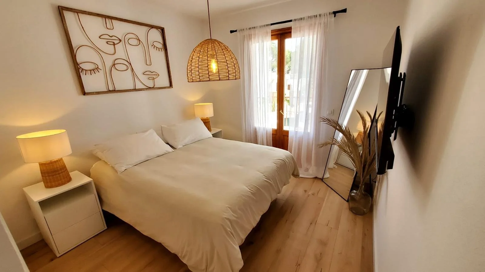 Habitación con cama, lámparas de noche, ventana con cortinas transparentes, espejo y decoración moderna decorada por seoane interiorismo en Mallorca. 