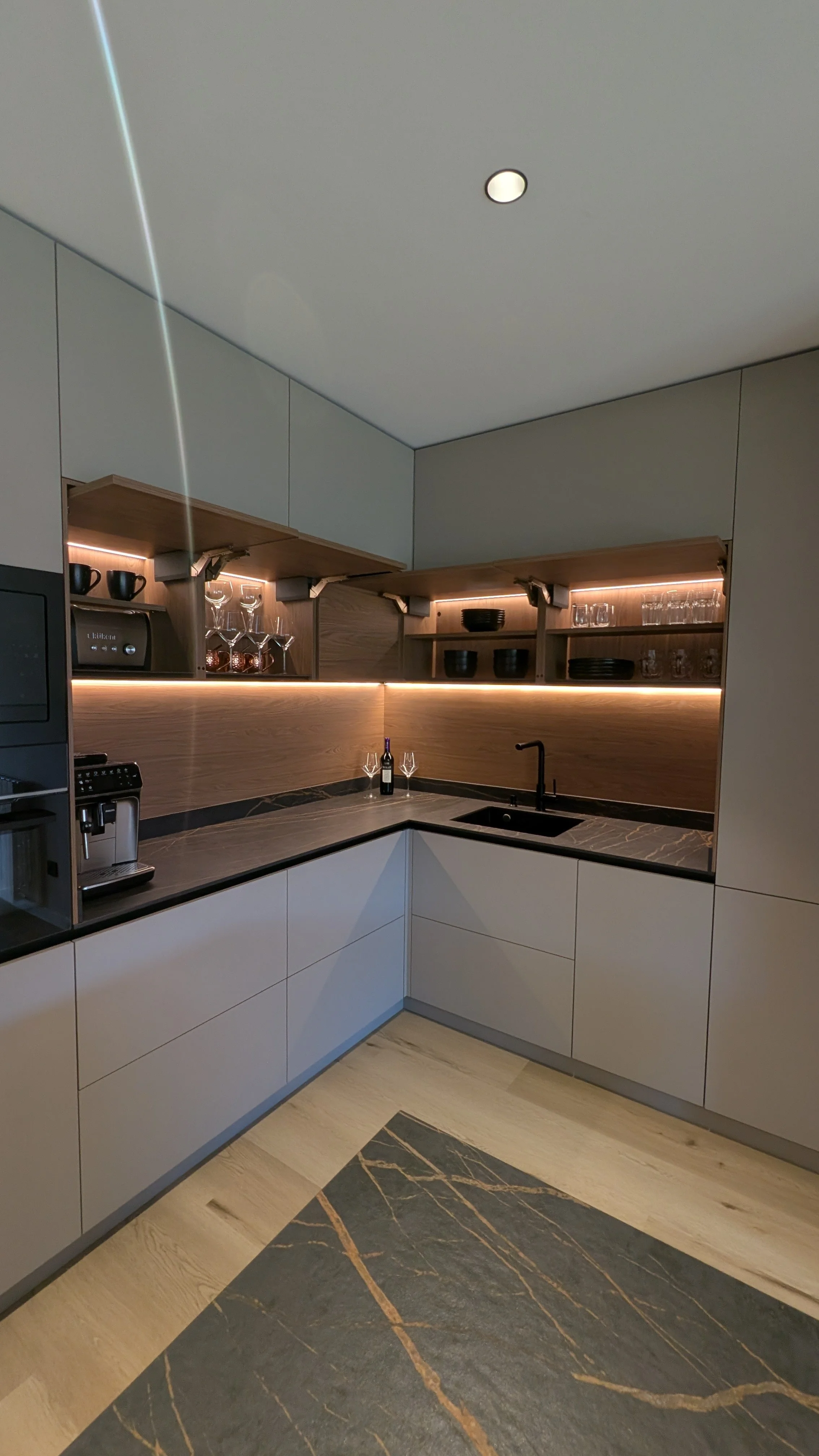Cocina moderna con gabinetes blancos, encimera de mármol negro y detalles de madera, con iluminación LED debajo de los gabinetes y utensilios de cocina en los estantes diseñada por seoane interiorismo en vitoria-gazteiz. 