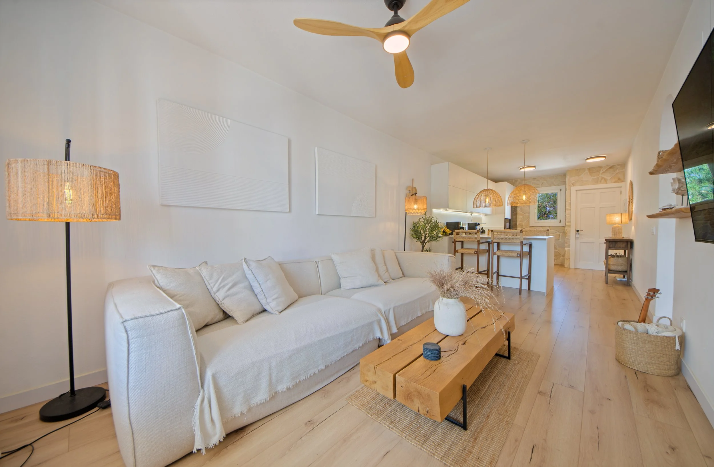 Seoaneinteriorismovitoriagazteizymallorca Sala de estar con sofá blanco, lámpara de pie, mesas de madera, paredes blancas con arte moderno, y decoración natural, en estilo minimalista y luminoso.