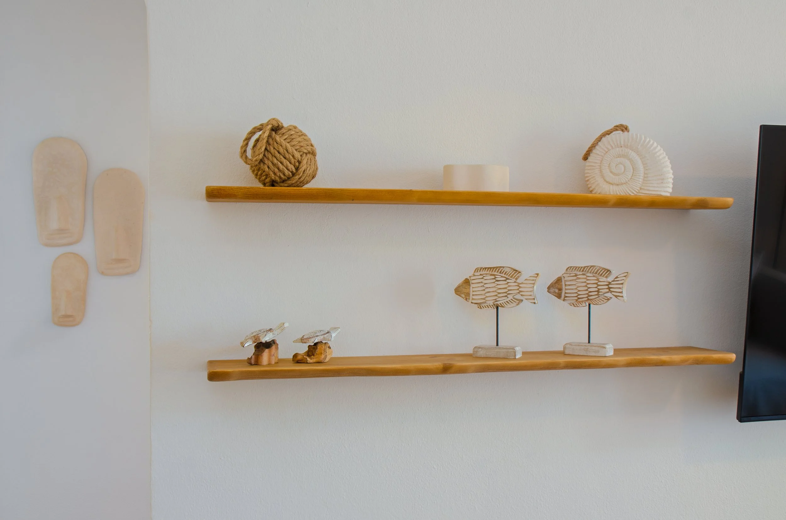 Decoración de pared con adornos de madera y objetos decorativos, incluyendo conchas, peces de madera y piezas de cerámica.