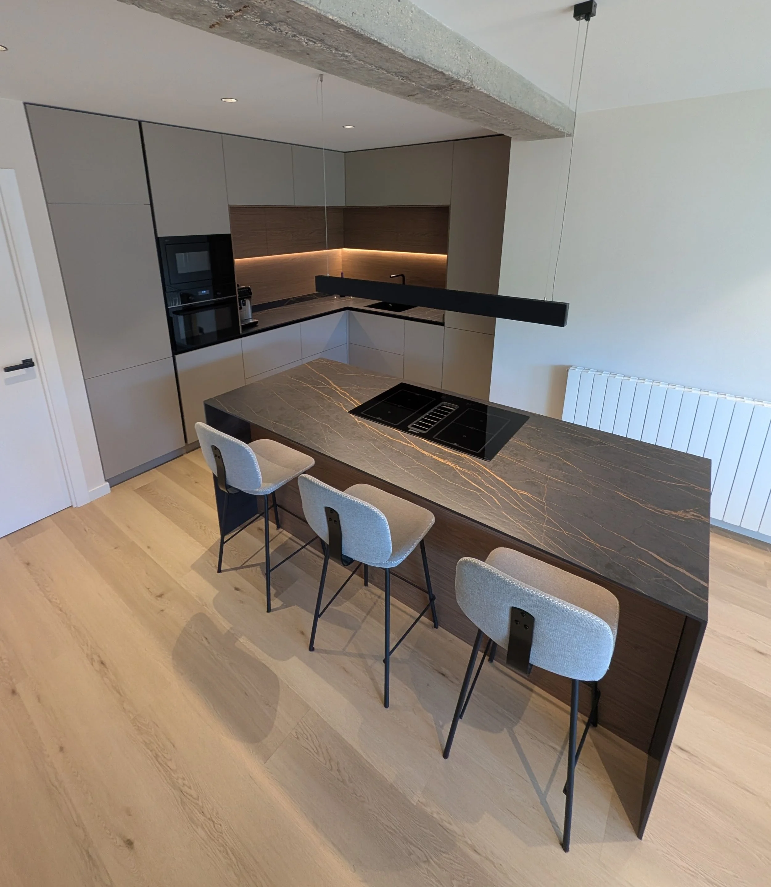 Cocina moderna con gabinetes grises y paredes de madera. Barra de cocina con encimera de piedra y sillas alrededor, iluminada con luces LED. Incluye electrodomésticos integrados y un extractor en la campana. diseño italiano vitoria-gazteiz. 