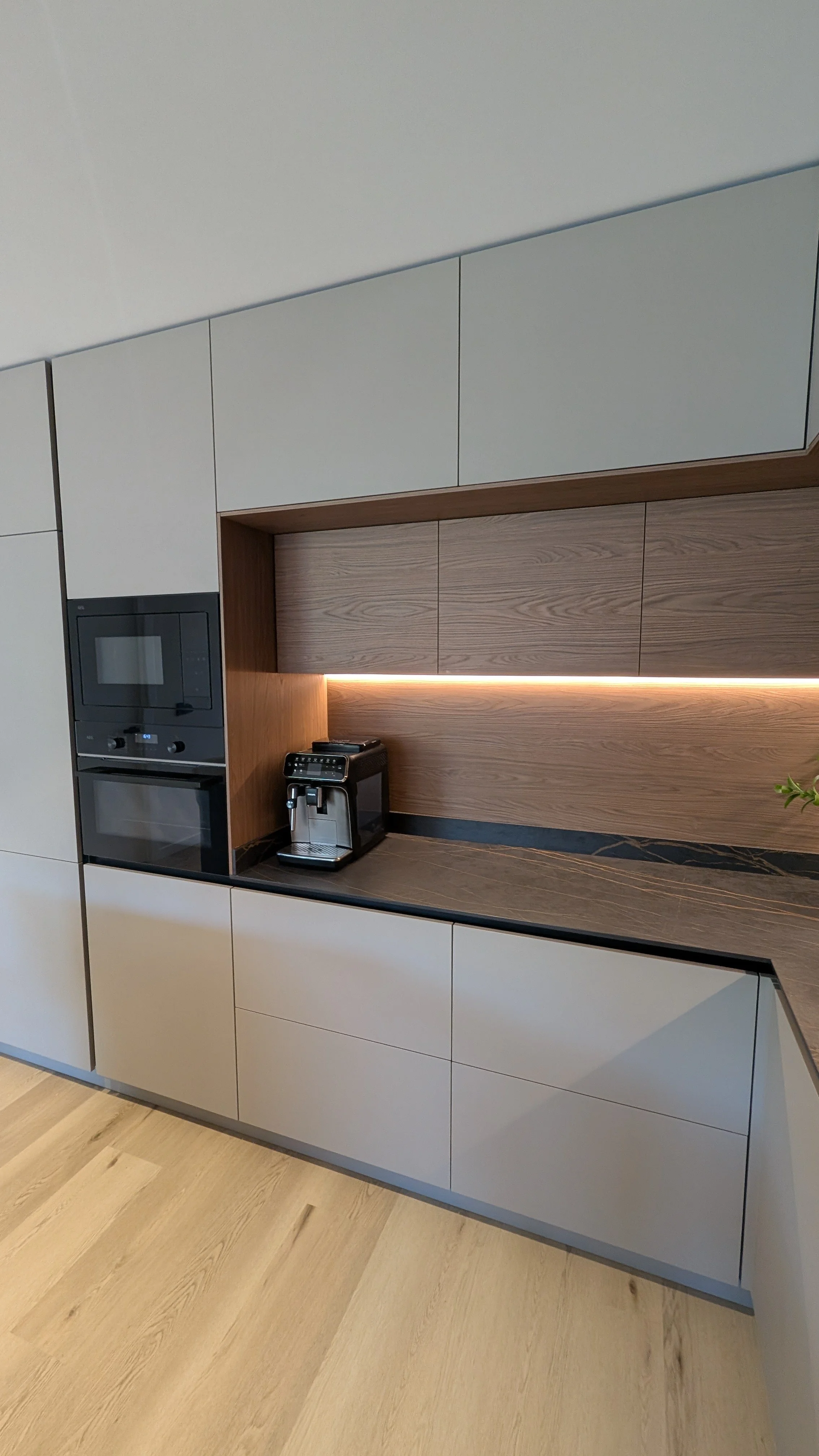 Cocina moderna con gabinetes blancos, mesa de mármol oscuro, cafetera espresso y horno empotrado fabricada y diseño italiano diseñado por Seoane interiorismo.