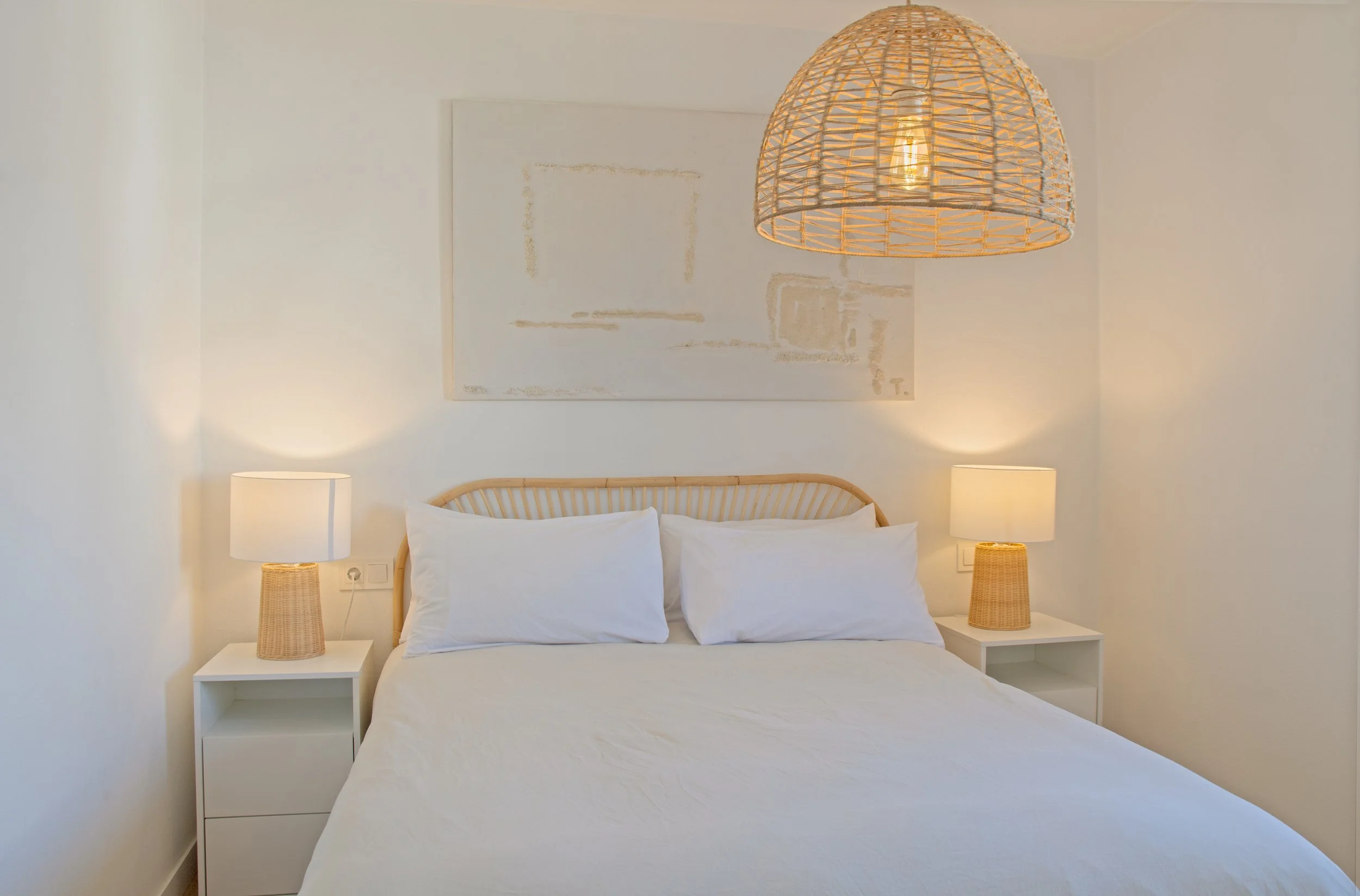 Cama con dos almohadas blancas en una habitación moderna con lámparas de noche y una lámpara de cesto