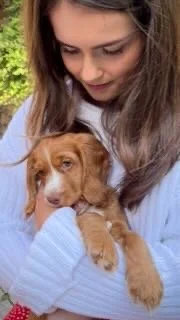 A young woman holding a small brown puppy outdoors
