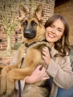 Young woman smiling and hugging a large German Shepherd dog outdoors near a brick building.