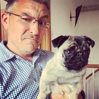 A man with glasses making a pouting face next to a small pug dog.