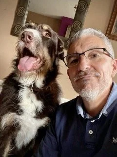 A man with glasses taking a selfie with a large brown and white dog indoors.
