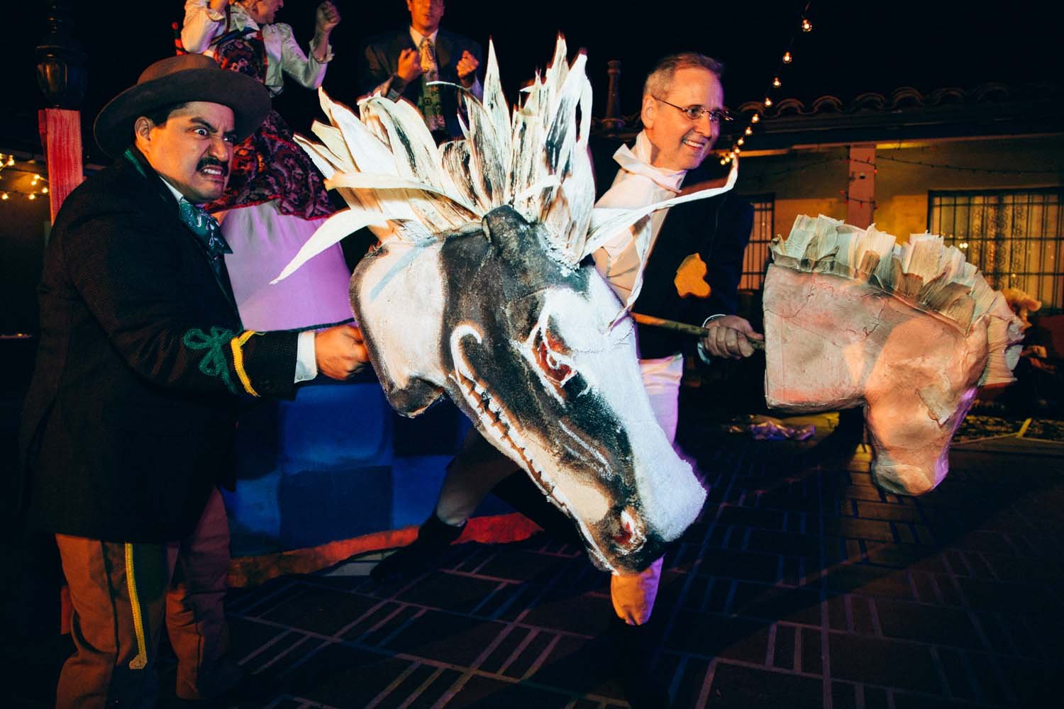 Actors from Señor Plummer's Final Fiesta by Rogue Artists Ensemble, participating in a traditional Mexican celebration, wearing costumes and holding a large, colorful papier-mâché horse head. Props by Lauren Marina of Tuzy Tuzy.