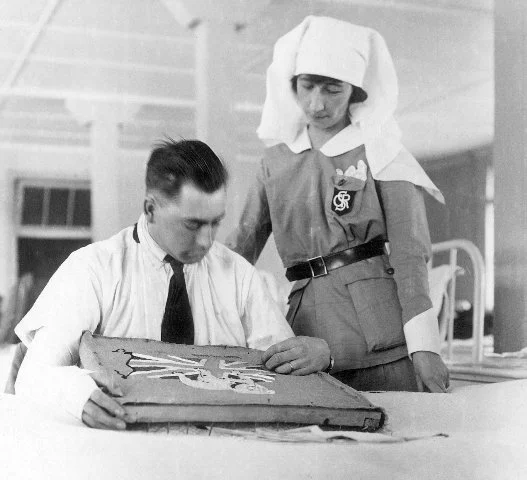 Graduate of Ward Aides Course working with a soldier injured in WWI. "SCR" on her lapel pocket stands for the Department of Soldier's Civil Re-establishment which oversaw the training program. 
