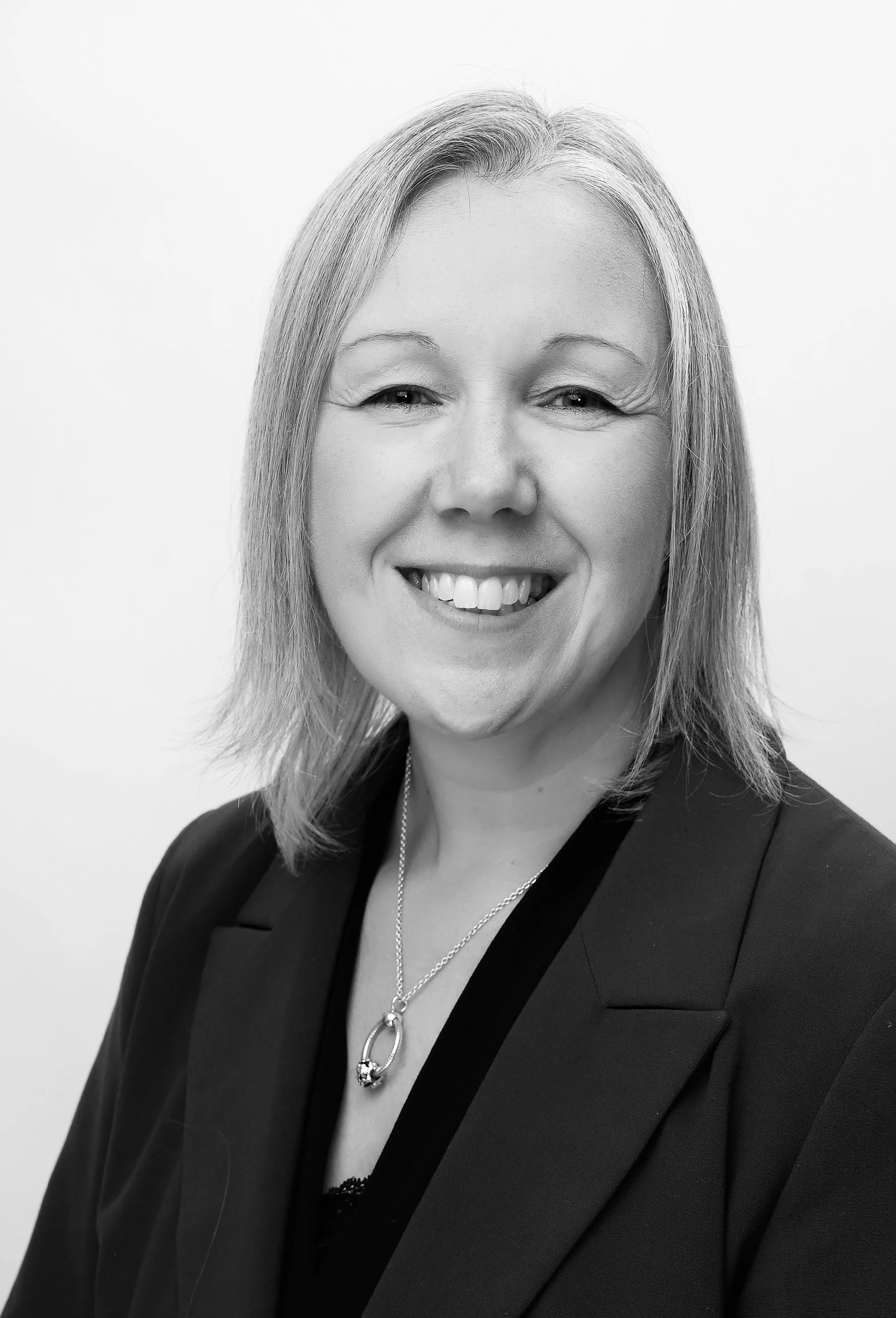 Black and white portrait of a smiling woman with shoulder-length hair, wearing a blazer and a necklace.