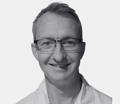 Black and white photo of a smiling man wearing glasses and a collared shirt.