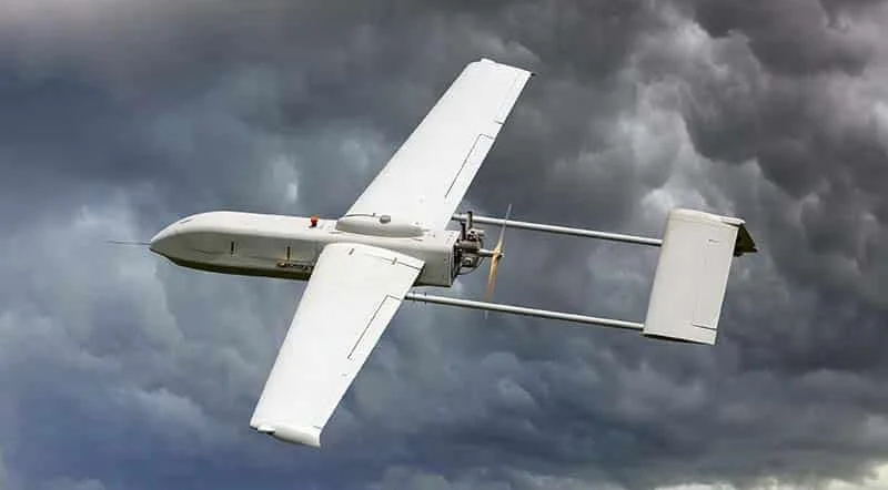 A white drone flying in a cloudy sky.