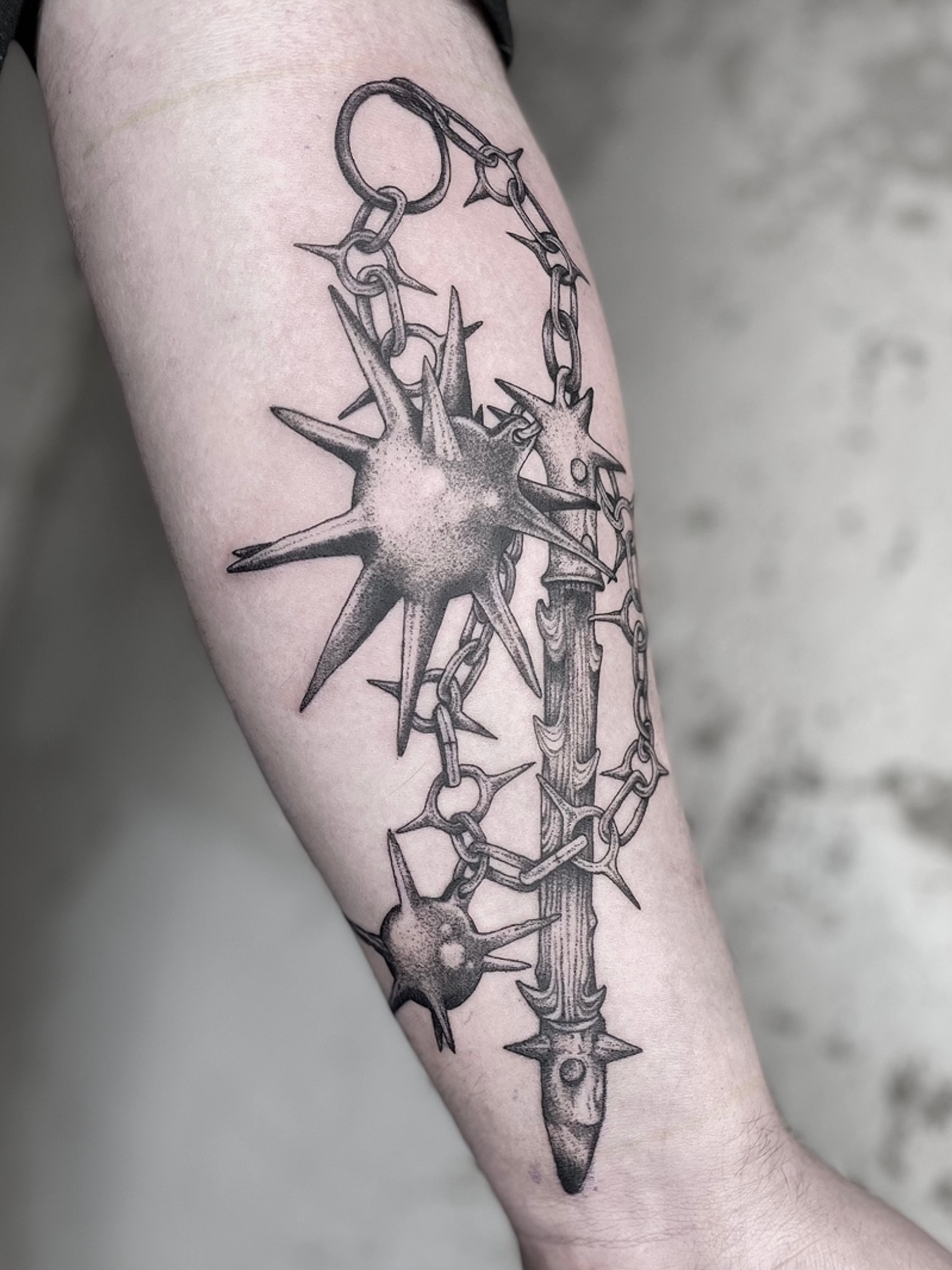 Black and gray tattoo of a detailed spiked mace and chain design on a person's forearm.