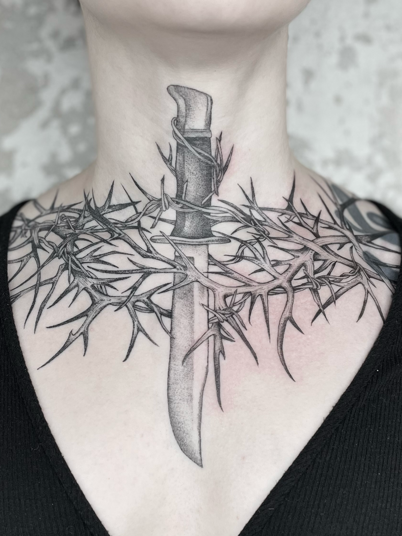 Tattoo of a sword surrounded by barbed wire on the person's neck and chest.