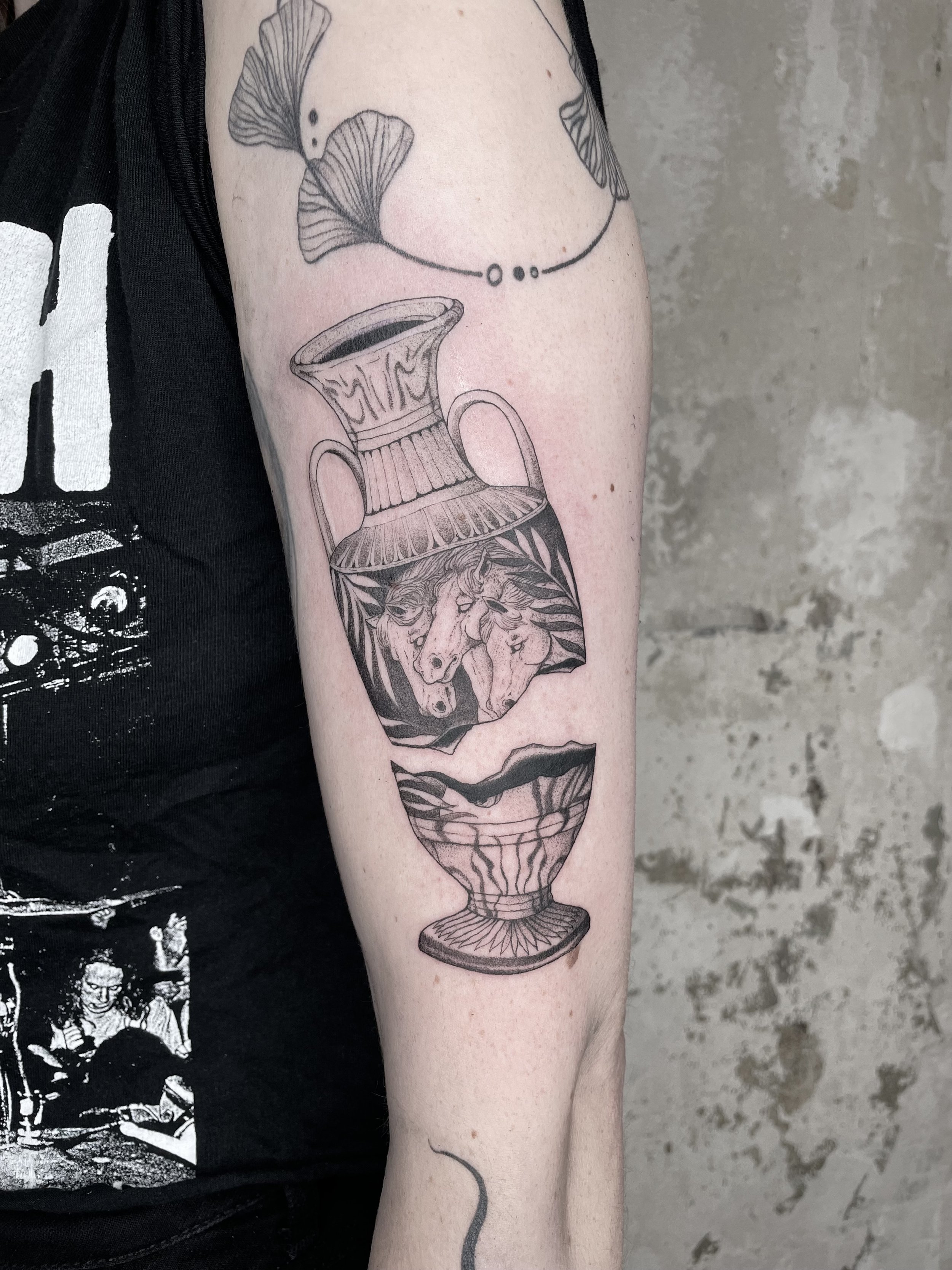 Tattoo of a decorative vase with a lion's head illustration, on person's upper arm.