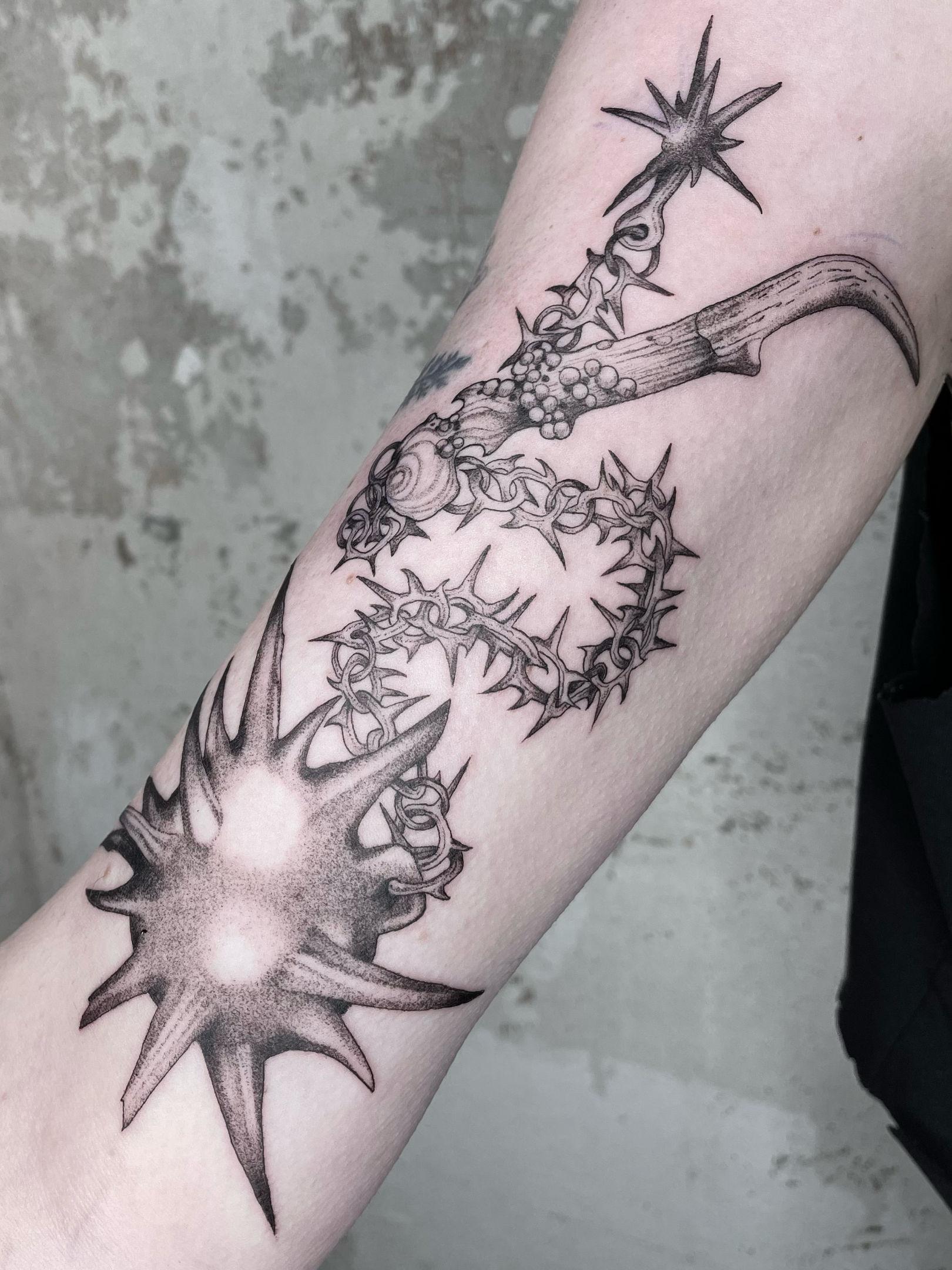 Black and gray tattoo of morningstar weapon and a thorny branch like chain wrapping around a part of the arm with detailed shading and texture.