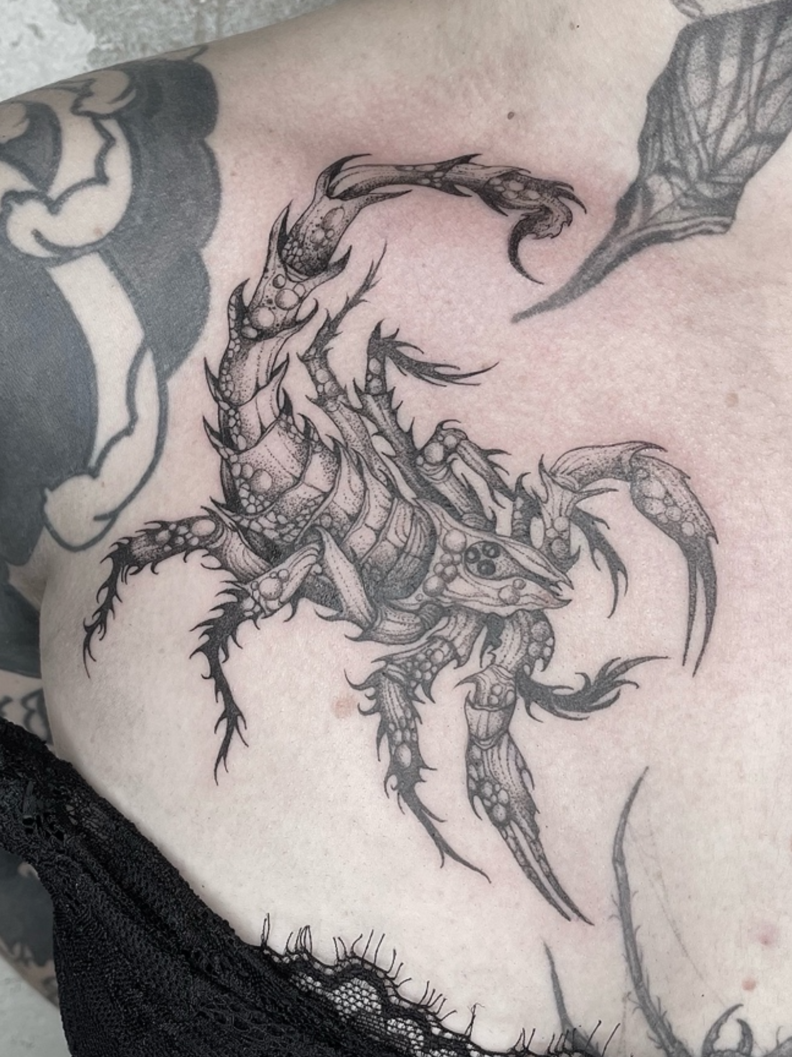 Tattoo of a scorpion on a person's skin, with detailed scales, claws, and wings, in black ink.