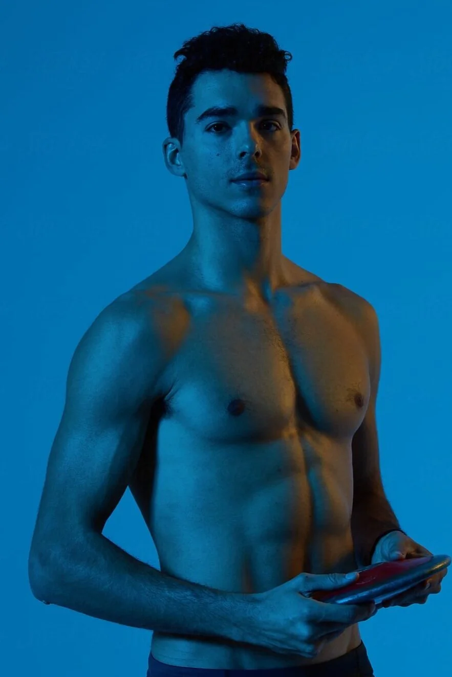 Joven desnudo sosteniendo una tableta, con fondo azul y iluminación de colores fríos y cálidos.