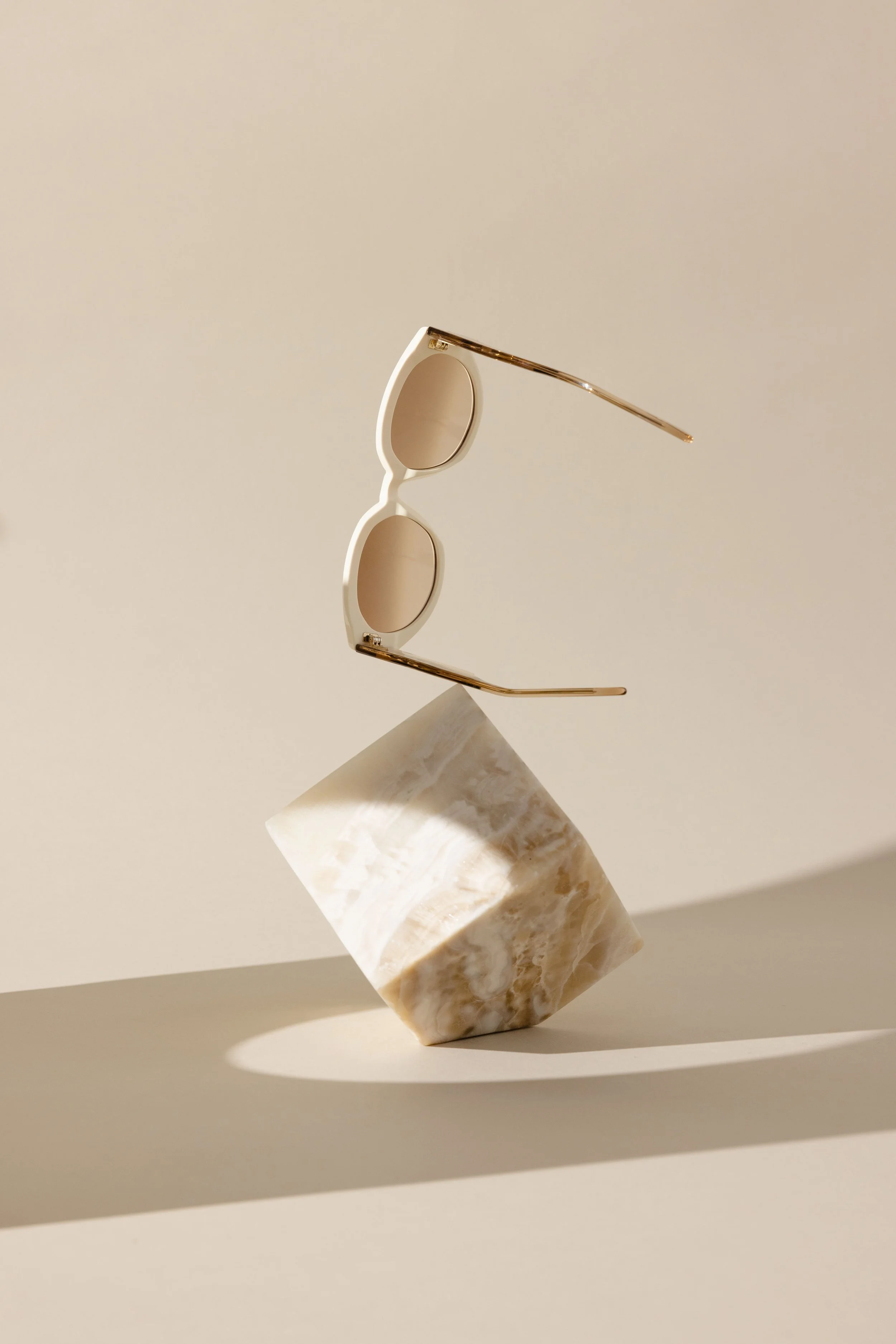 Sonnenbrille, die über einem beigen Marmorwürfel schwebt