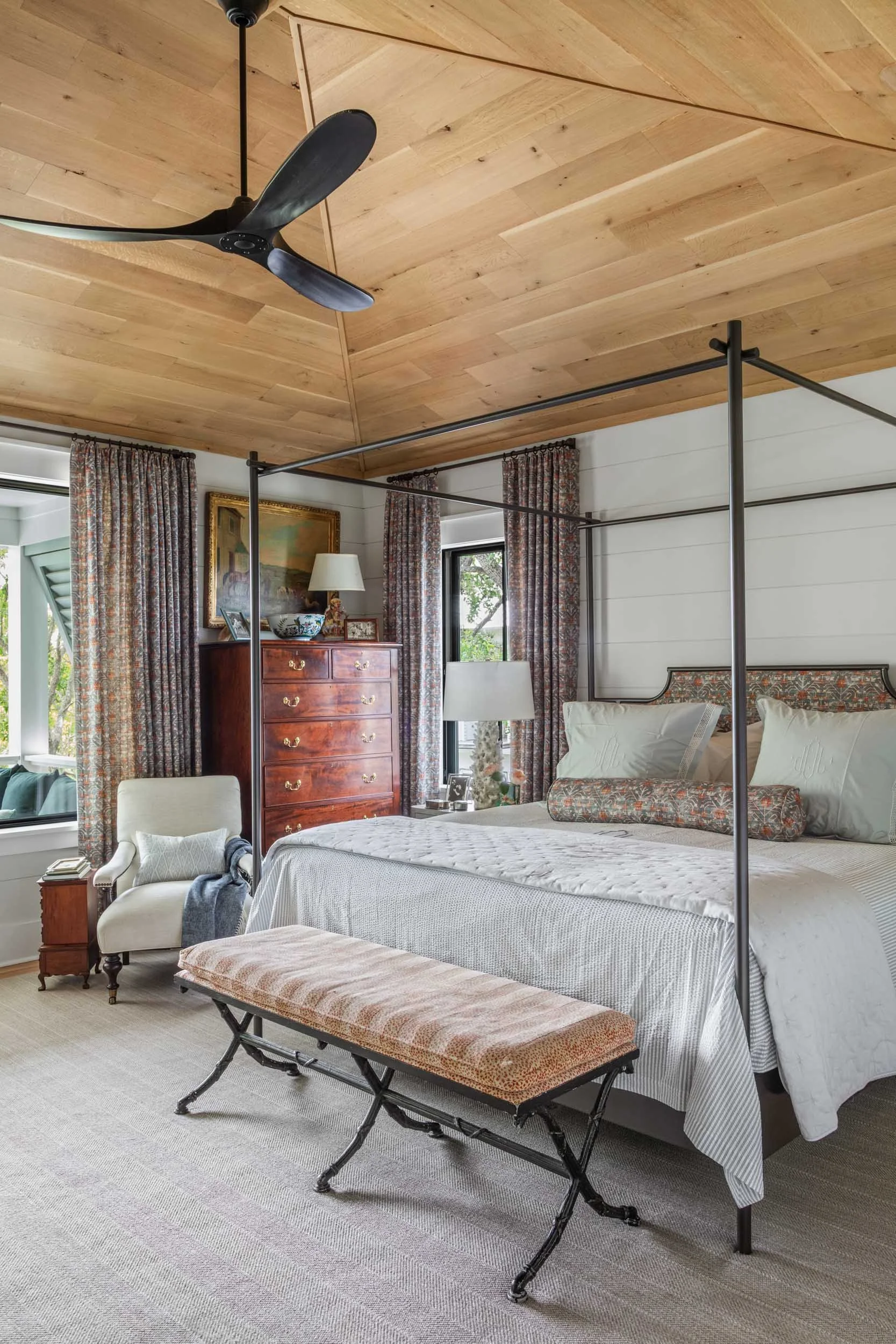 primary-bedroom-custom-iron-bed-upholstered-headboard-matching-curtains-oil-rubbed-bronze-ticking-bedspread-monogrammed linens-coral-lamps-linen-shades-upholstered-iron-bench.jpg