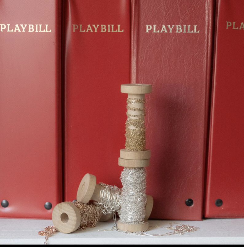 Stacked wooden spools with glittery and chain decorations in front of red Playbill folders.