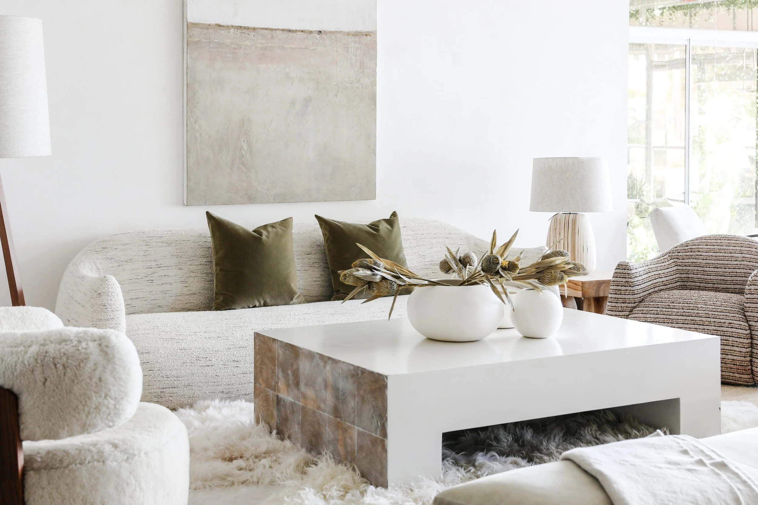 Living room with neutral-colored furniture, a white coffee table with decorative vases, and a large window with natural light.