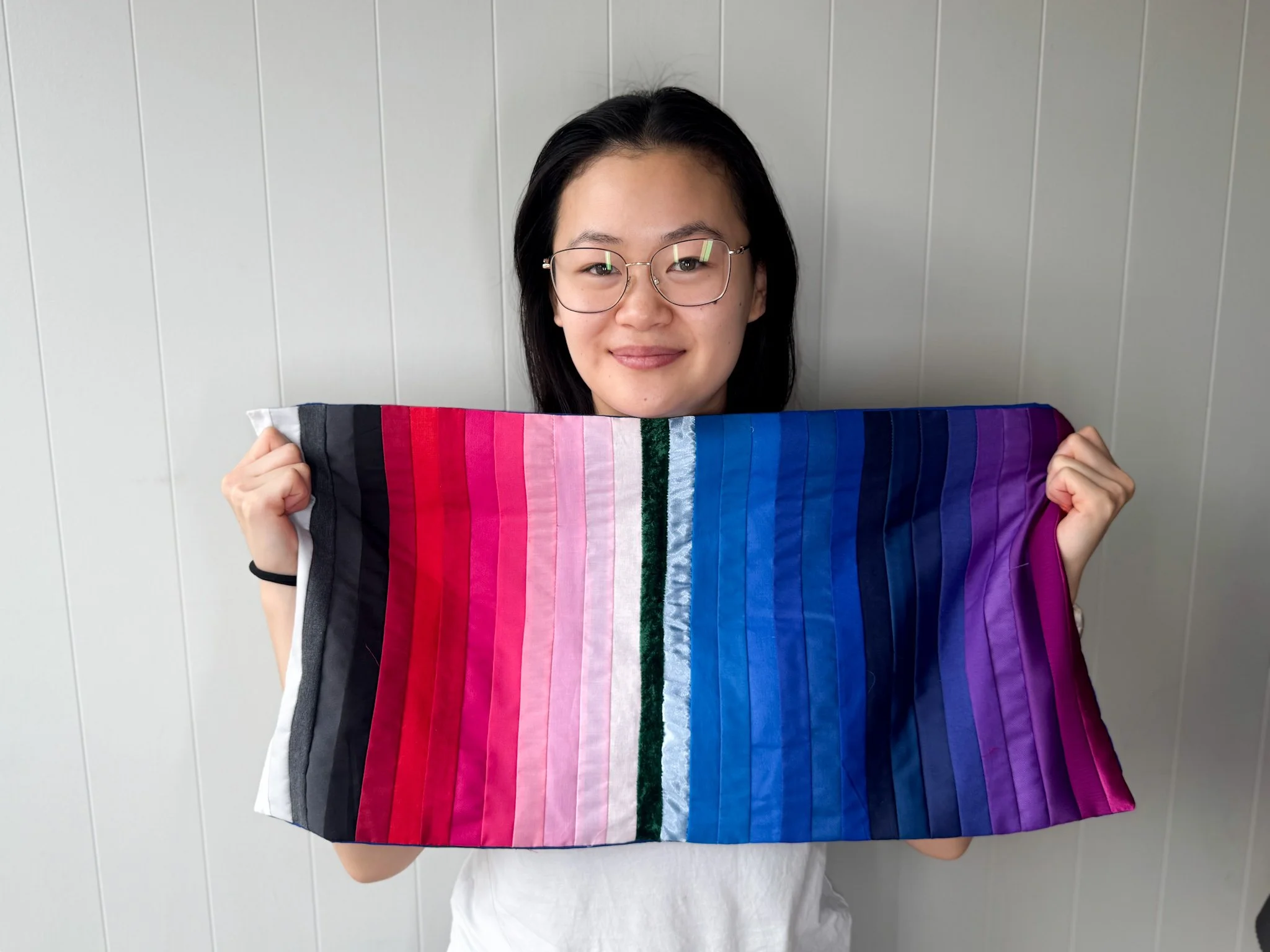 En kvinne med briller holder opp True Winter-farger foran ansiktet. Stoffet har tynne, fargerike striper og vises mot en lys vegg