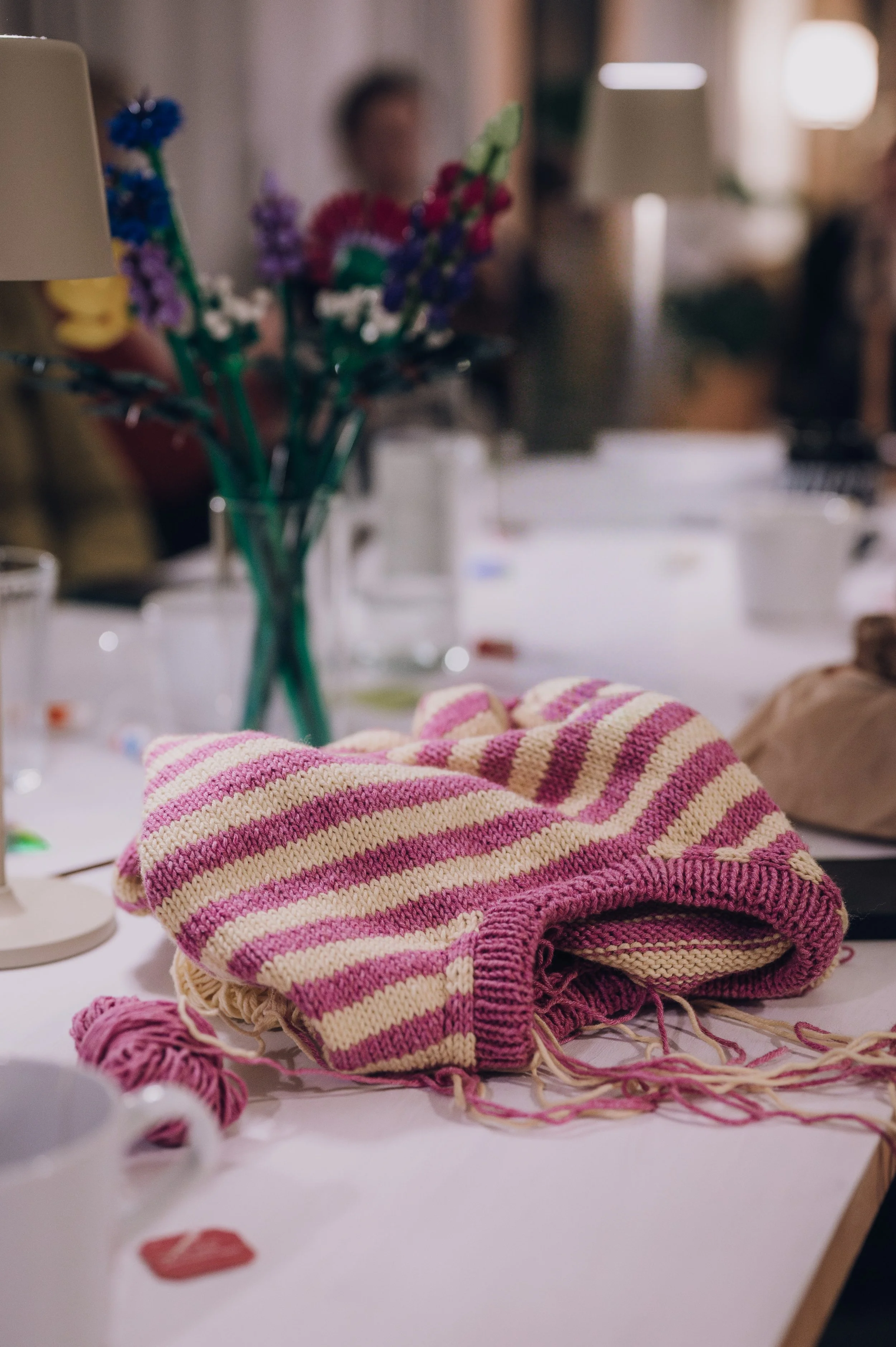 Strickrunde am großen Tisch mit Garn, Getränken und Notizen bei einem Strickkurs für Freundinnen.