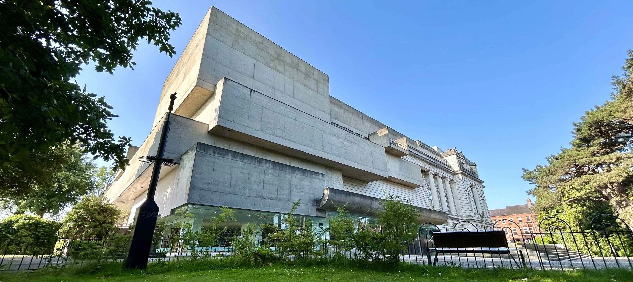 Modern concrete building with large overhangs, surrounded by trees and green space, under a clear blue sky.