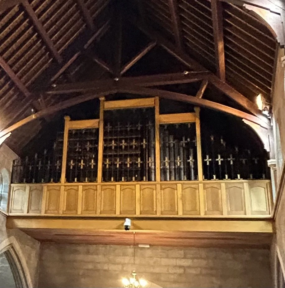 Wooden choir loft with decorative metal railings and a dark vaulted wooden ceiling inside a church.