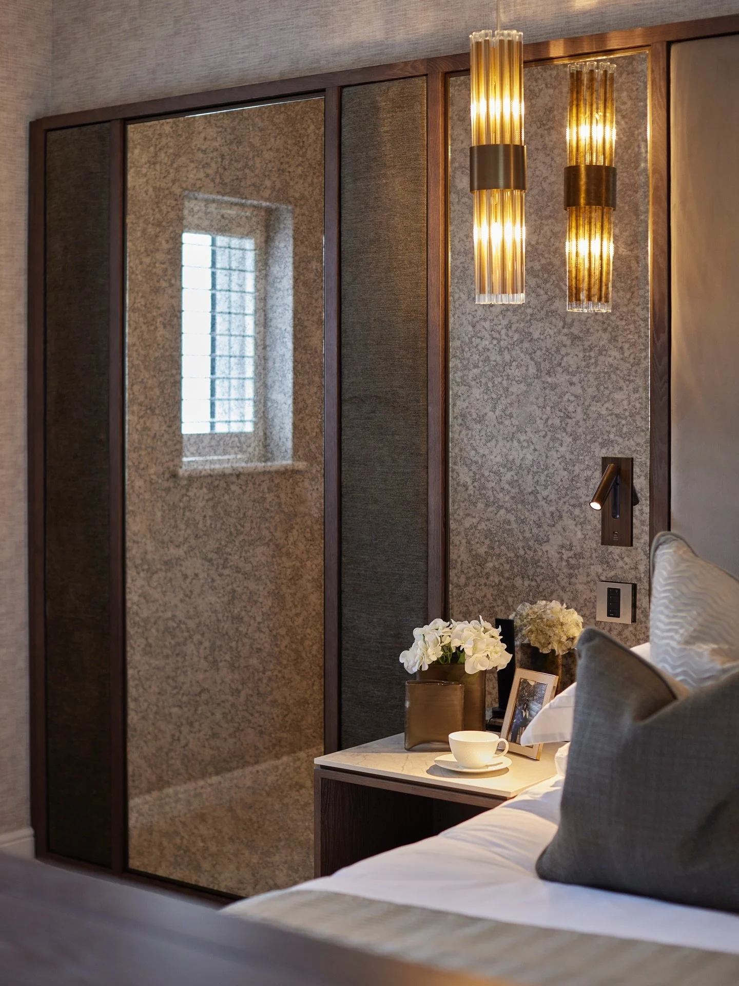 The Master Headboard at Hawthorn House features thoughtful detailing to create a full hotel-suite feel. 
Layered materials, antique mirror, inset reading lights, decorative pendants and bespoke bedside tables all come together to form the perfect tra